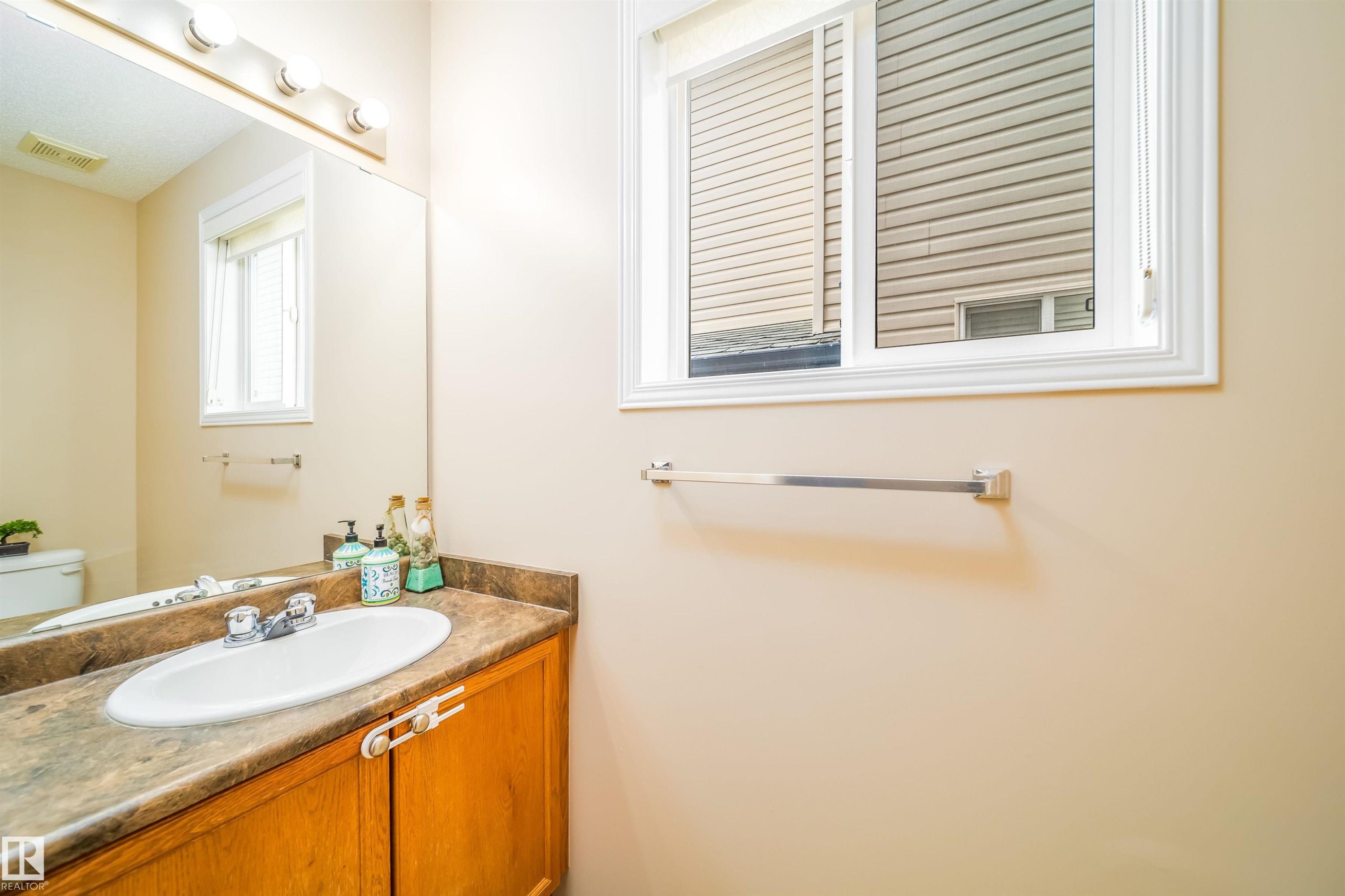 Well-appointed bathroom featuring a vanity with a countertop and integrated sink, a large mirror, and a window providing natural light - 8932 175 Avenue, Edmonton, AB - Indoor Photo Showing Bathroom