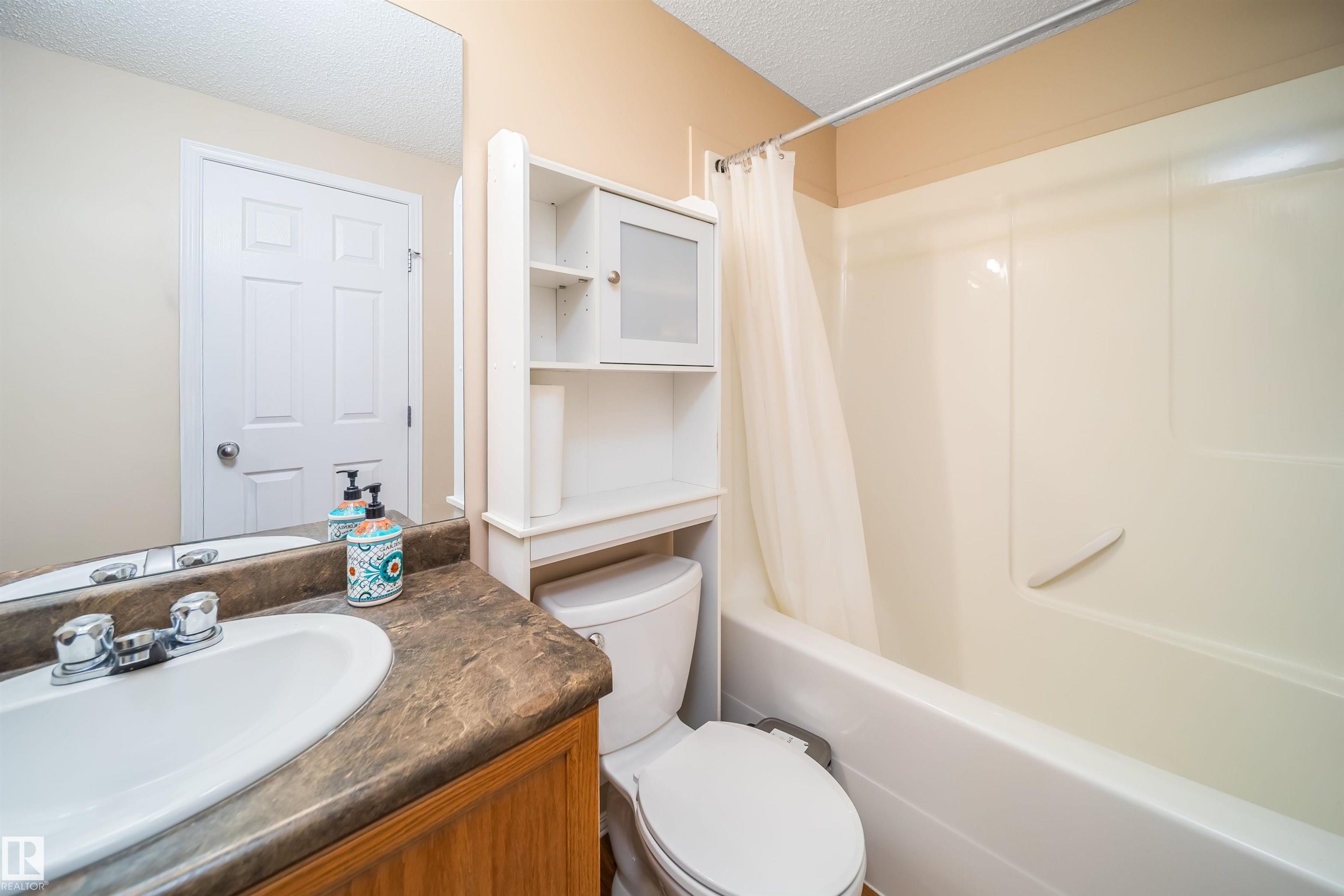 Bathroom featuring a vanity with a white basin and a brown countertop, a toilet, a white storage unit, and a bathtub with a shower curtain - 8932 175 Avenue, Edmonton, AB - Indoor Photo Showing Bathroom