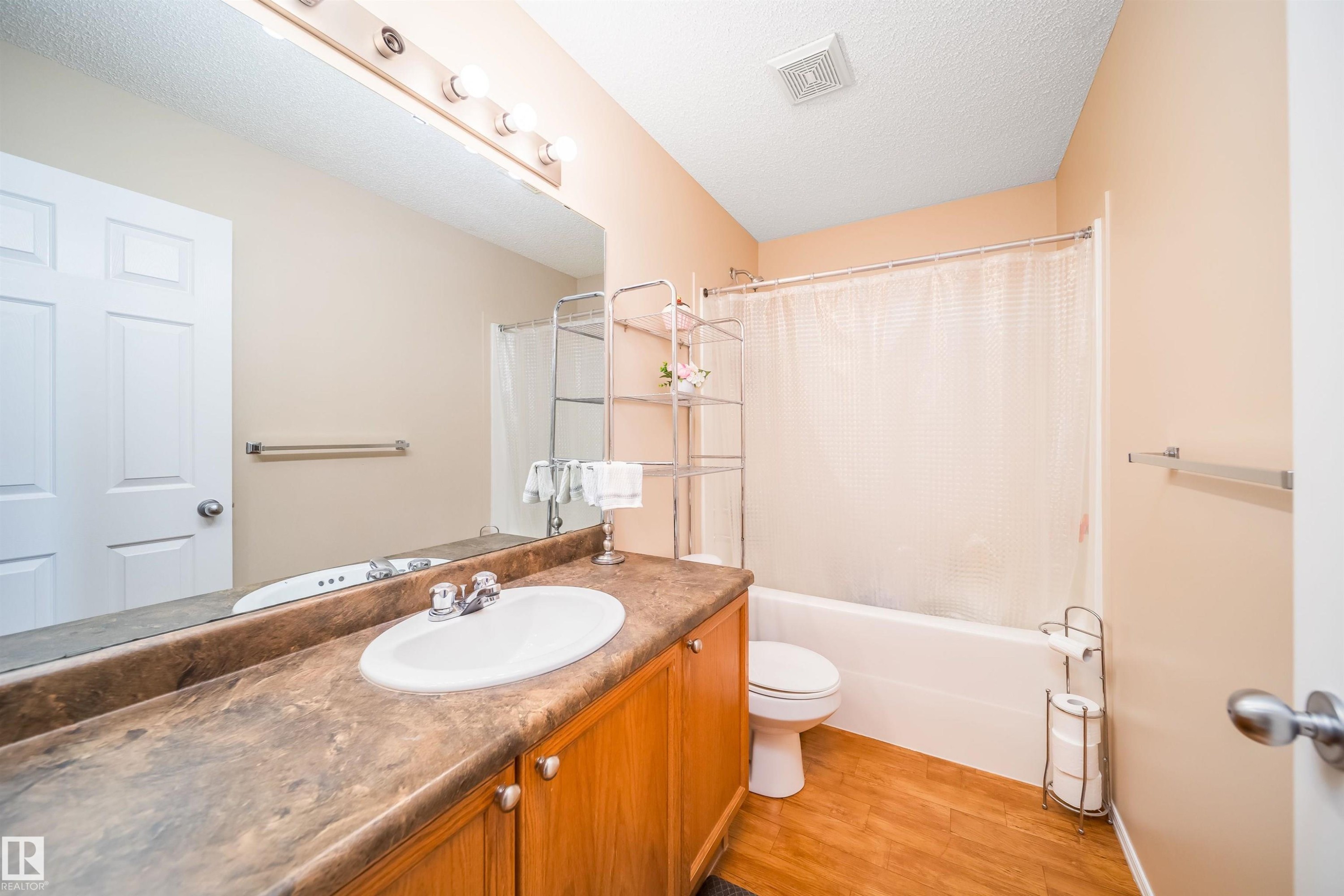 Bathroom featuring a vanity with a laminate countertop and a drop-in sink, a bathtub with a shower, and wood-look flooring - 8932 175 Avenue, Edmonton, AB - Indoor Photo Showing Bathroom