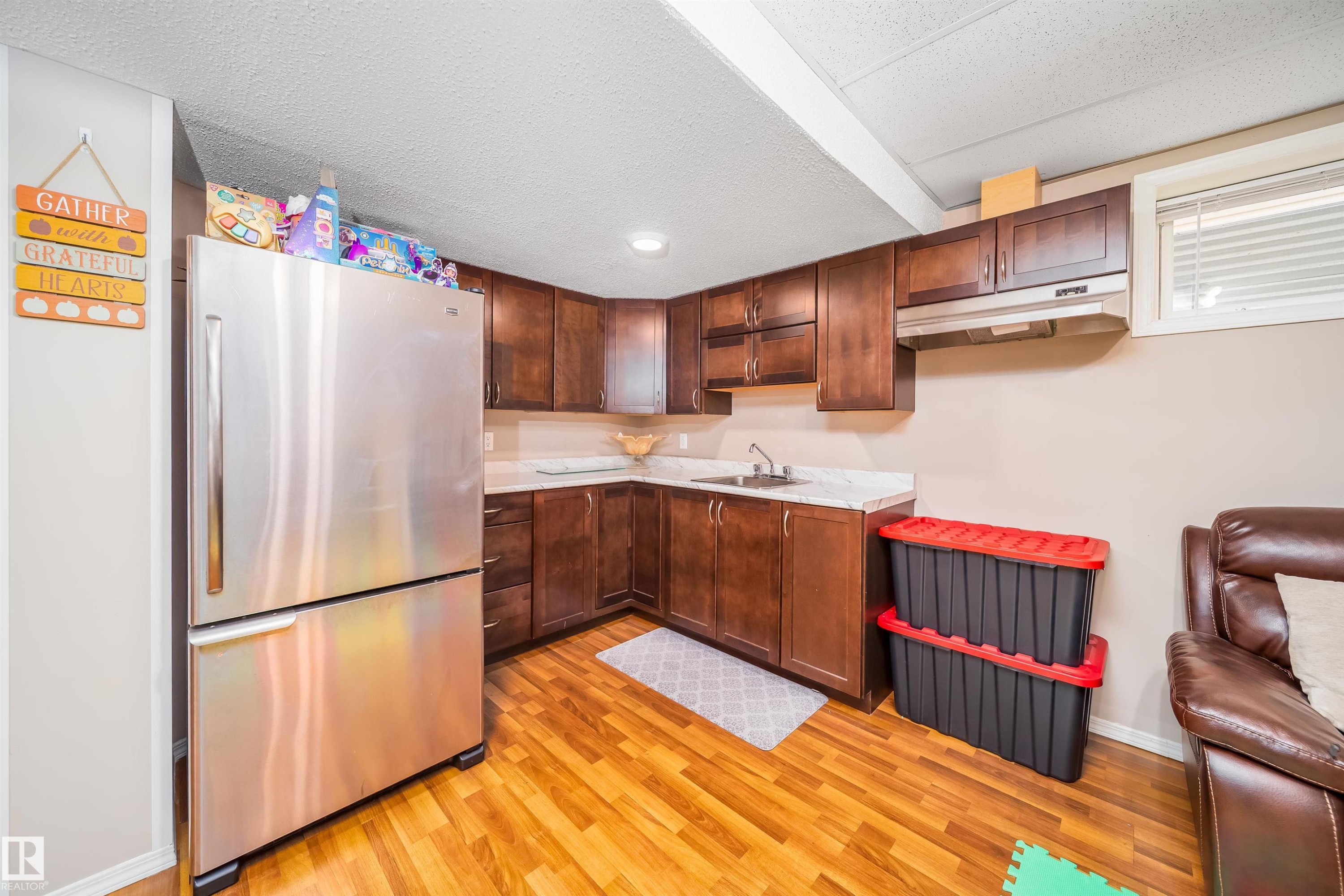 The property features a kitchen area with wood flooring, dark wood cabinetry, a stainless steel refrigerator, and a sink with a countertop - 8932 175 Avenue, Edmonton, AB - Indoor Photo Showing Kitchen