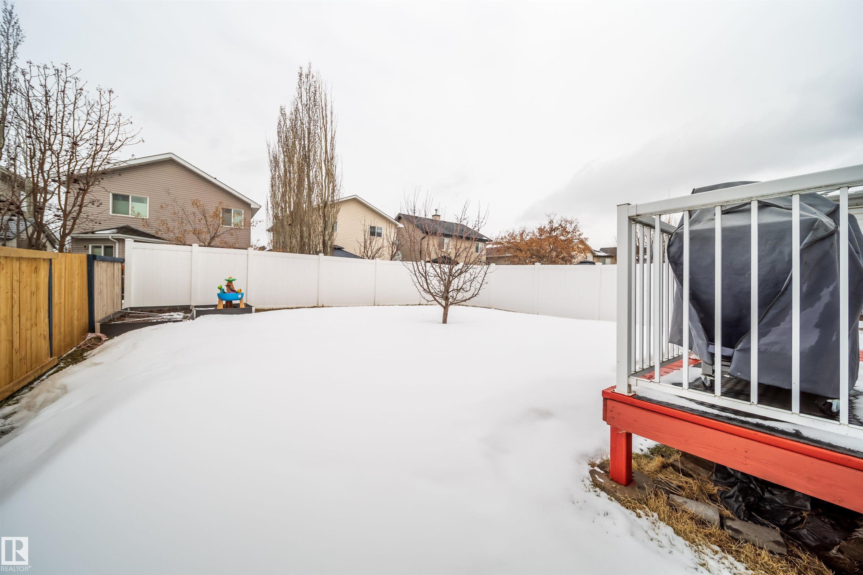 The property features a spacious yard with a white privacy fence and a red deck with white railings - 8932 175 Avenue, Edmonton, AB - Outdoor