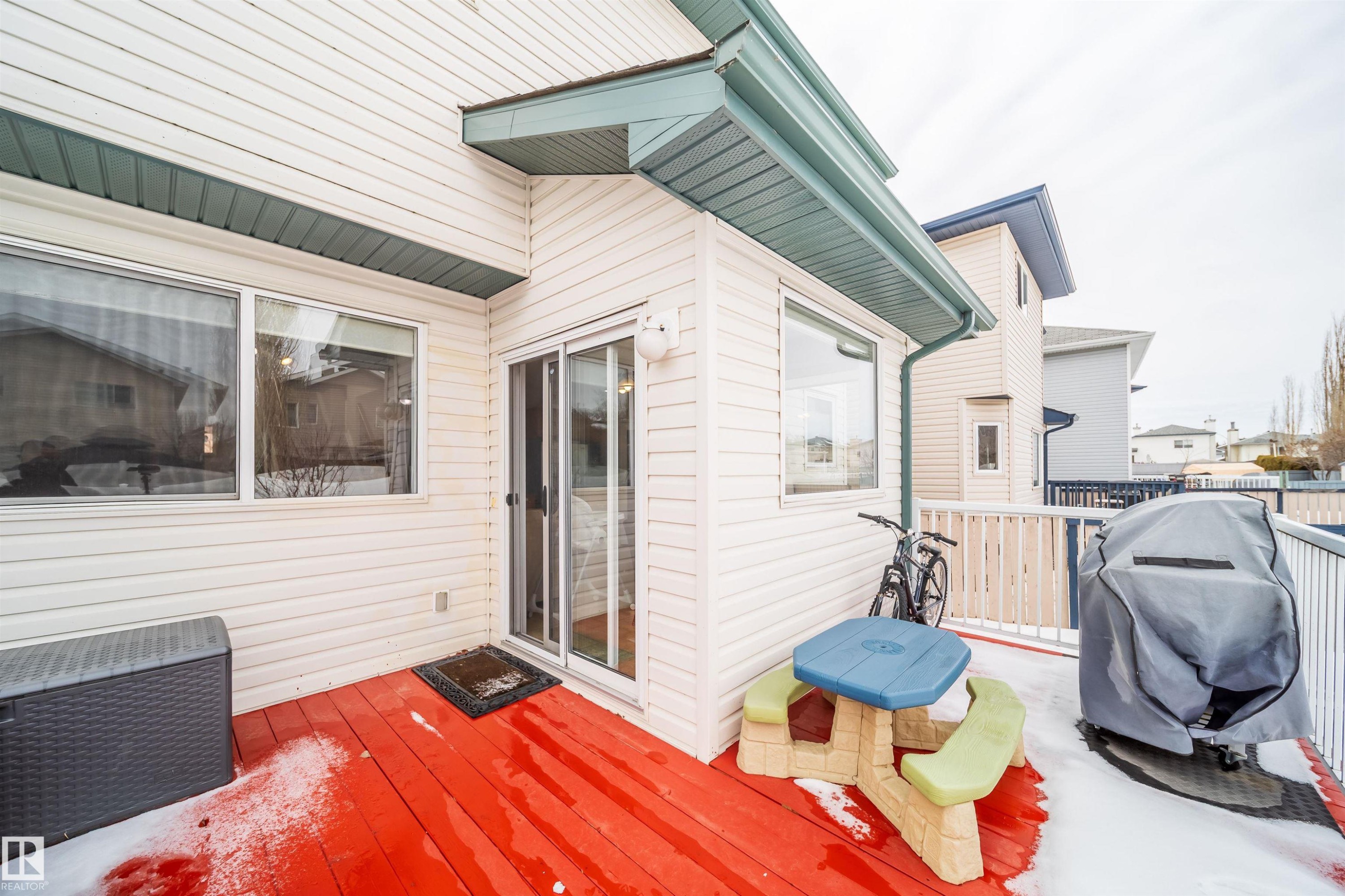 The property features a red deck with a white railing, white siding, and a sliding glass door - 8932 175 Avenue, Edmonton, AB - Outdoor With Deck Patio Veranda With Exterior