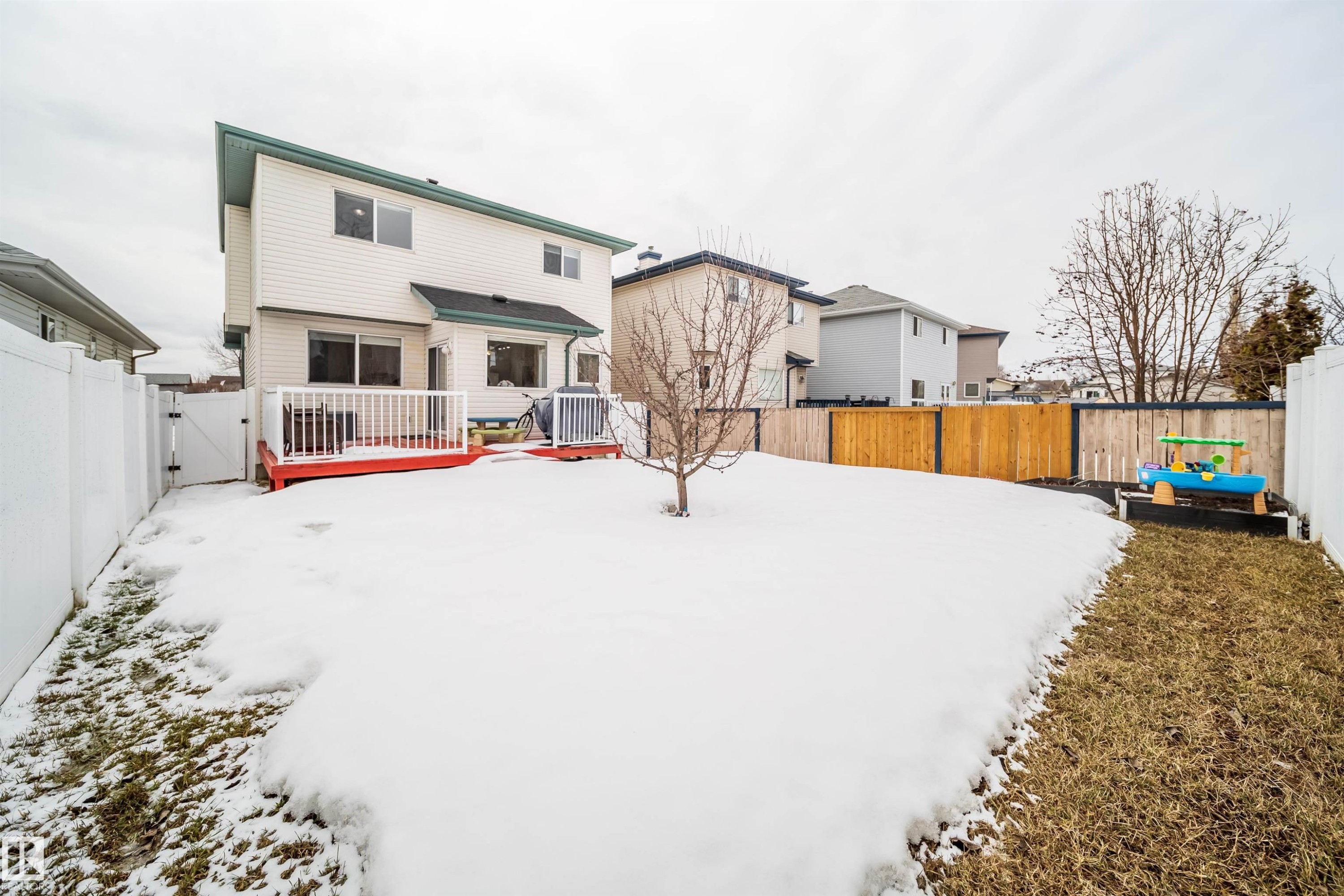 The property features a white exterior with a red deck overlooking a fenced yard - 8932 175 Avenue, Edmonton, AB - Outdoor