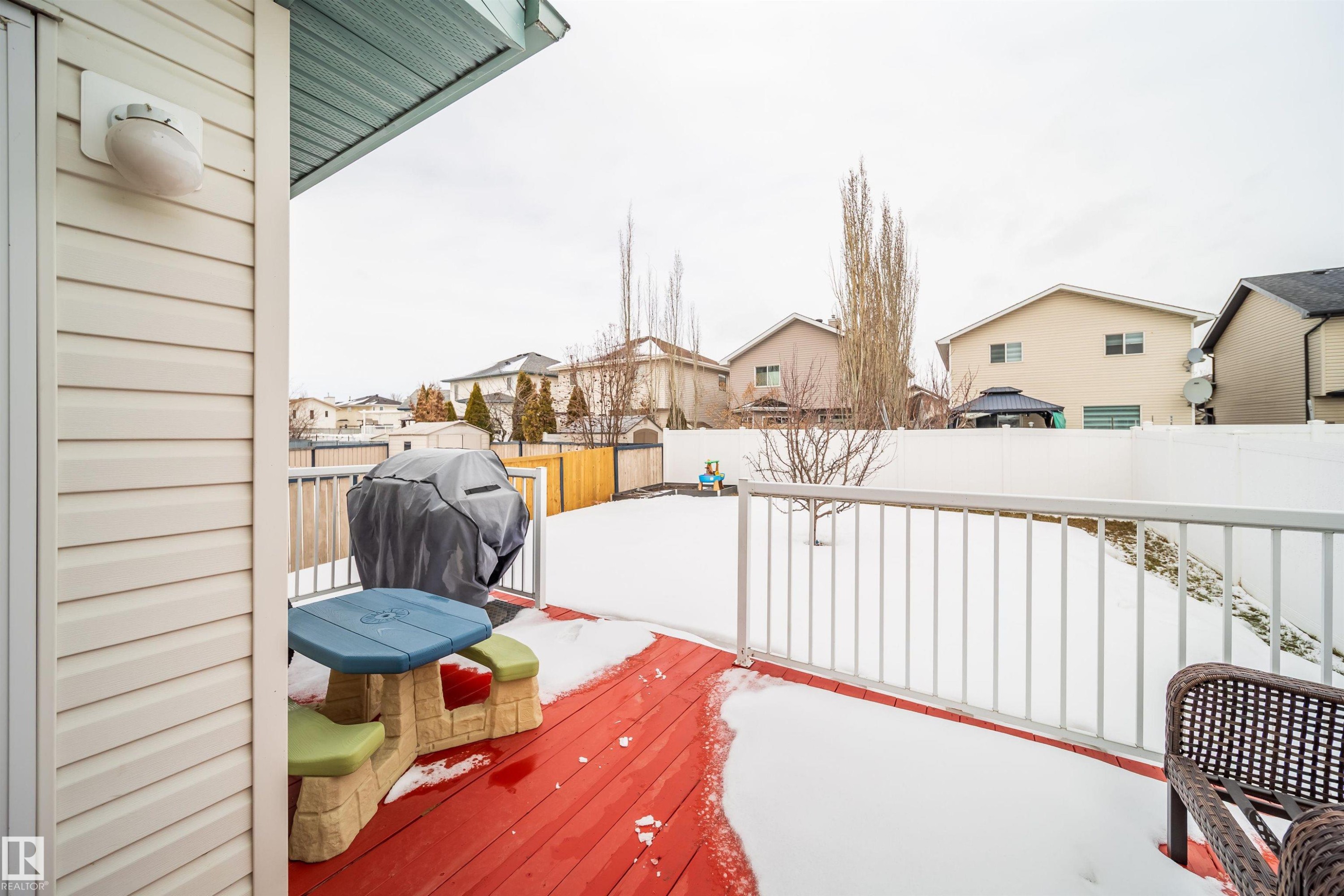 The property features a red wooden deck with a white railing, overlooking a snow-covered yard - 8932 175 Avenue, Edmonton, AB - Outdoor With Exterior