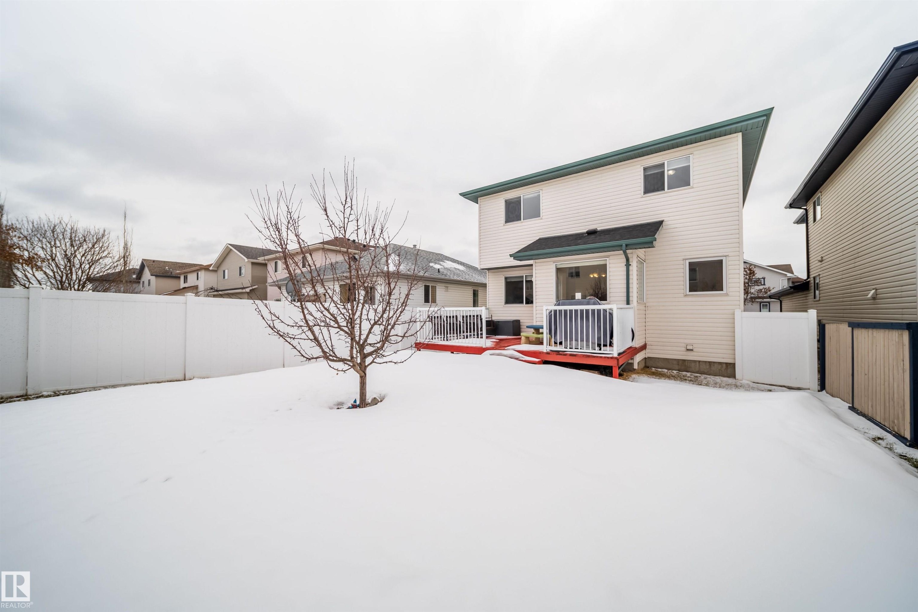The property features a spacious backyard with a deck, a white fence, and a bare tree - 8932 175 Avenue, Edmonton, AB - Outdoor With Deck Patio Veranda