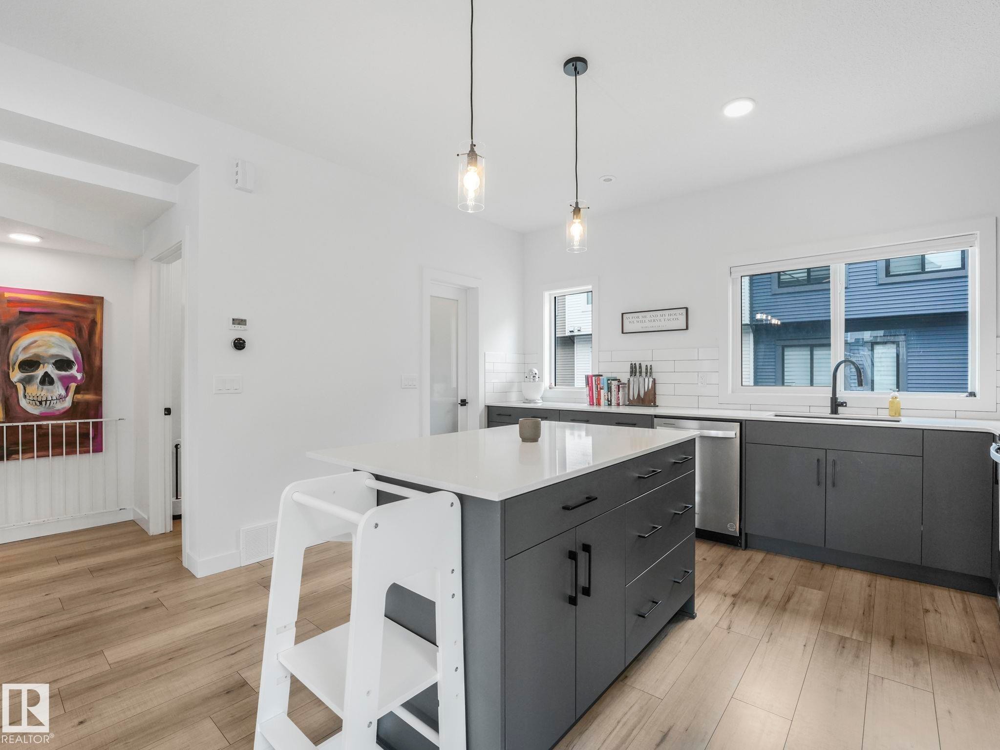 The kitchen features an island with a light-colored countertop, dark cabinetry, and light wood-look flooring - 95 1010 Rabbit Hill Road, Edmonton, AB - Indoor Photo Showing Kitchen With Upgraded Kitchen