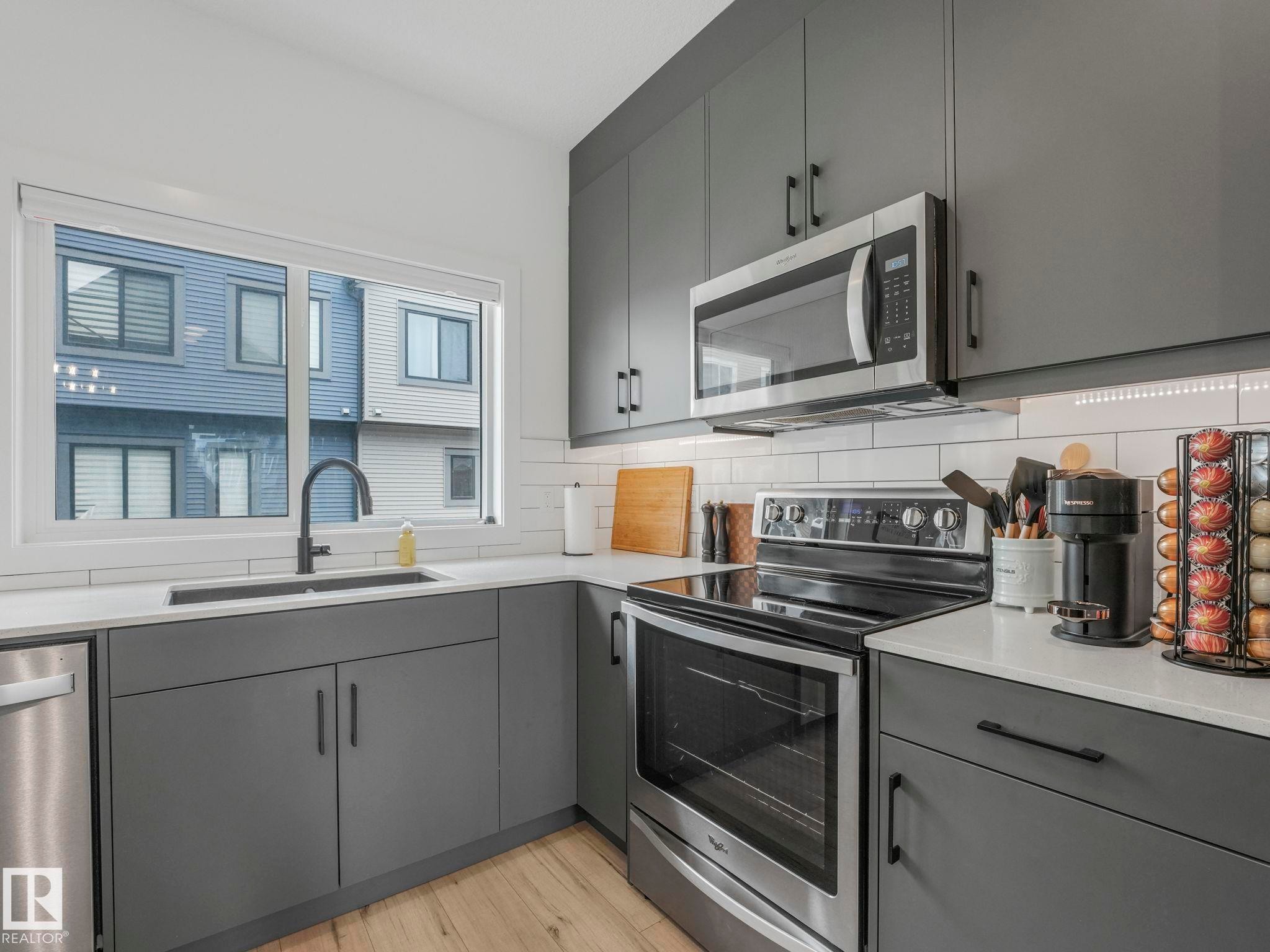 The kitchen features gray cabinetry with black hardware, a stainless steel microwave, and an electric range - 95 1010 Rabbit Hill Road, Edmonton, AB - Indoor Photo Showing Kitchen With Double Sink
