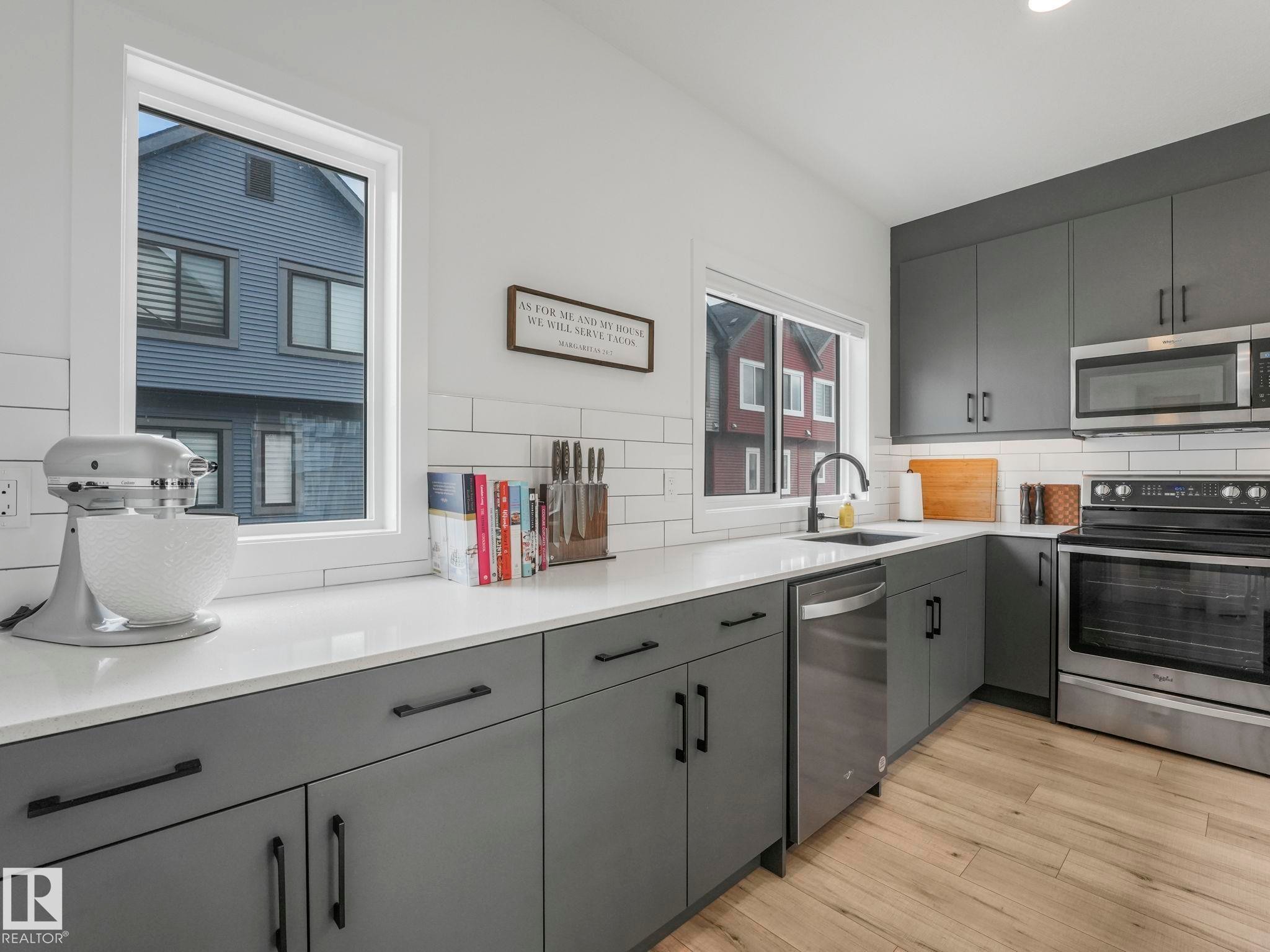 The kitchen features grey cabinetry, stainless steel appliances, and a white subway tile backsplash, all complemented by light wood-style flooring - 95 1010 Rabbit Hill Road, Edmonton, AB - Indoor Photo Showing Kitchen