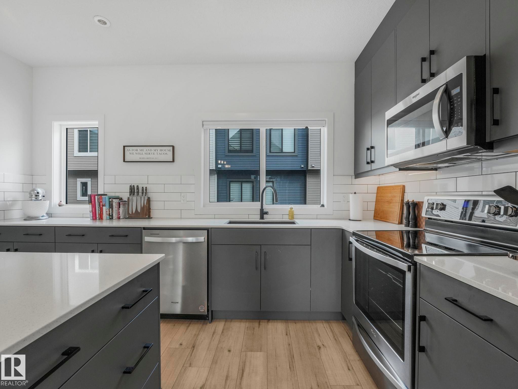 Modern kitchen featuring dark grey cabinetry, white countertops, stainless steel appliances, and light wood flooring - 95 1010 Rabbit Hill Road, Edmonton, AB - Indoor Photo Showing Kitchen