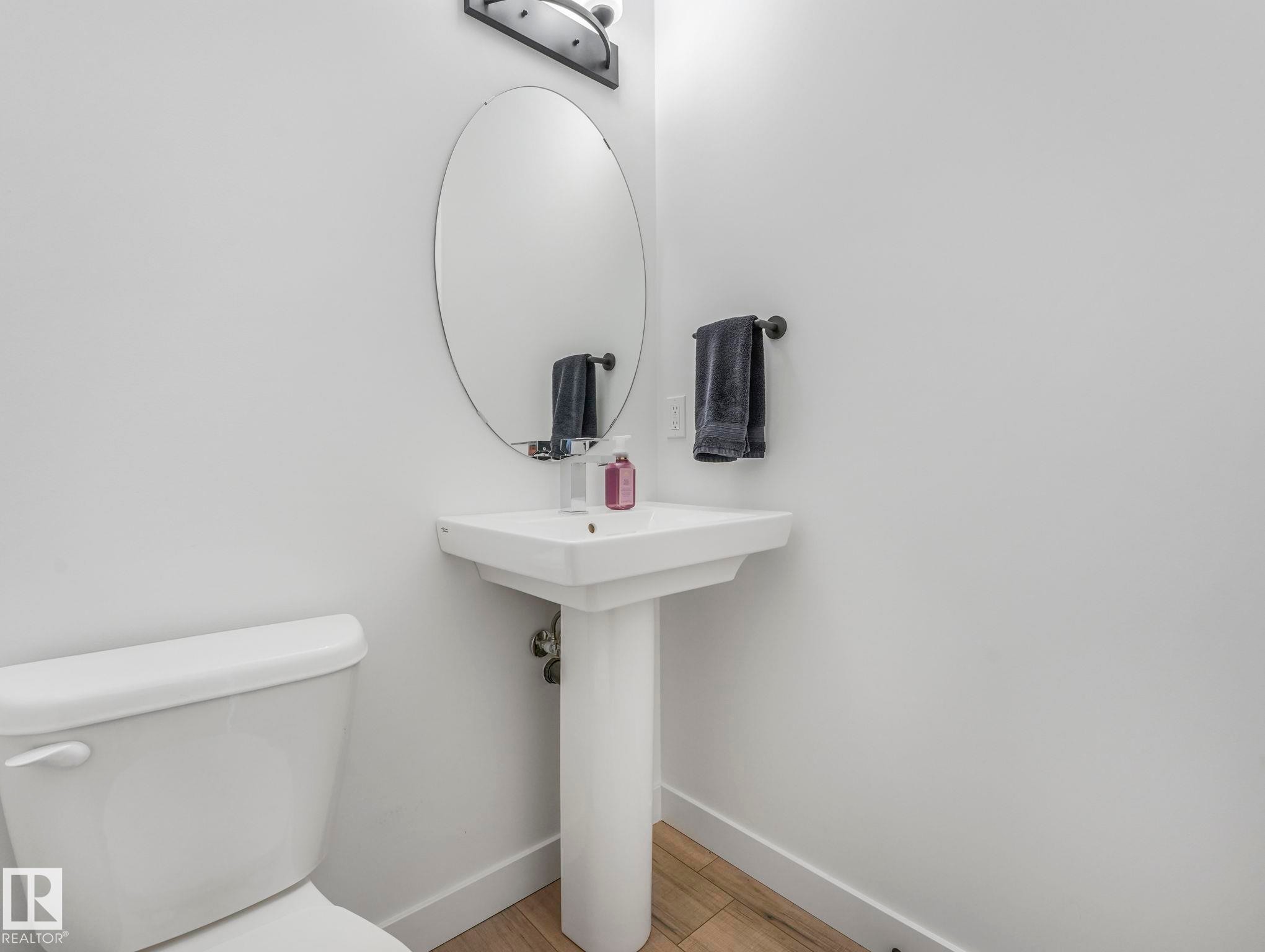 This bathroom features a white pedestal sink with a mirror above it, a wall-mounted towel rack, and a white toilet - 95 1010 Rabbit Hill Road, Edmonton, AB - Indoor Photo Showing Bathroom