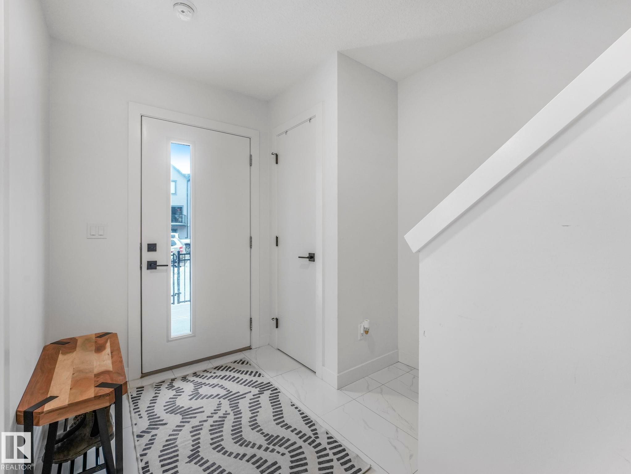 Inviting entryway featuring a white front door with a vertical window pane, tiled flooring, and a white staircase with a prominent handrail - 95 1010 Rabbit Hill Road, Edmonton, AB - Indoor Photo Showing Other Room