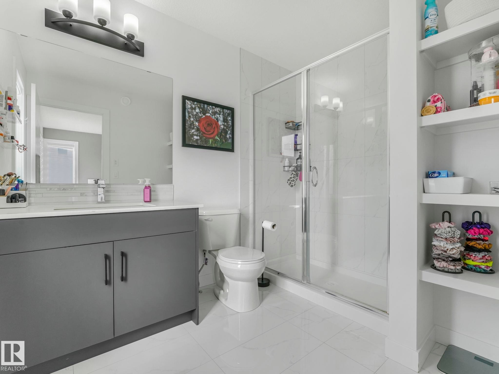 This bathroom features a contemporary gray vanity with a white countertop, a spacious walk-in shower with a glass enclosure, and built-in shelving providing additional storage - 95 1010 Rabbit Hill Road, Edmonton, AB - Indoor Photo Showing Bathroom