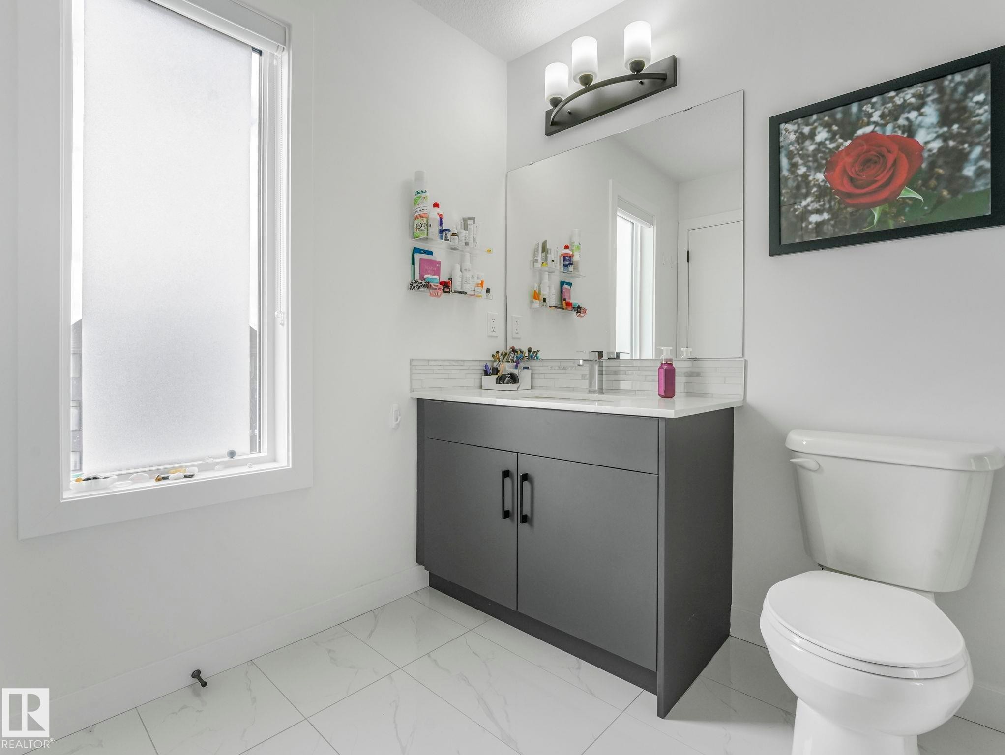 Bathroom with a window featuring frosted glass, a vanity with a dark grey cabinet and white countertop, a mirror, and a toilet - 95 1010 Rabbit Hill Road, Edmonton, AB - Indoor Photo Showing Bathroom