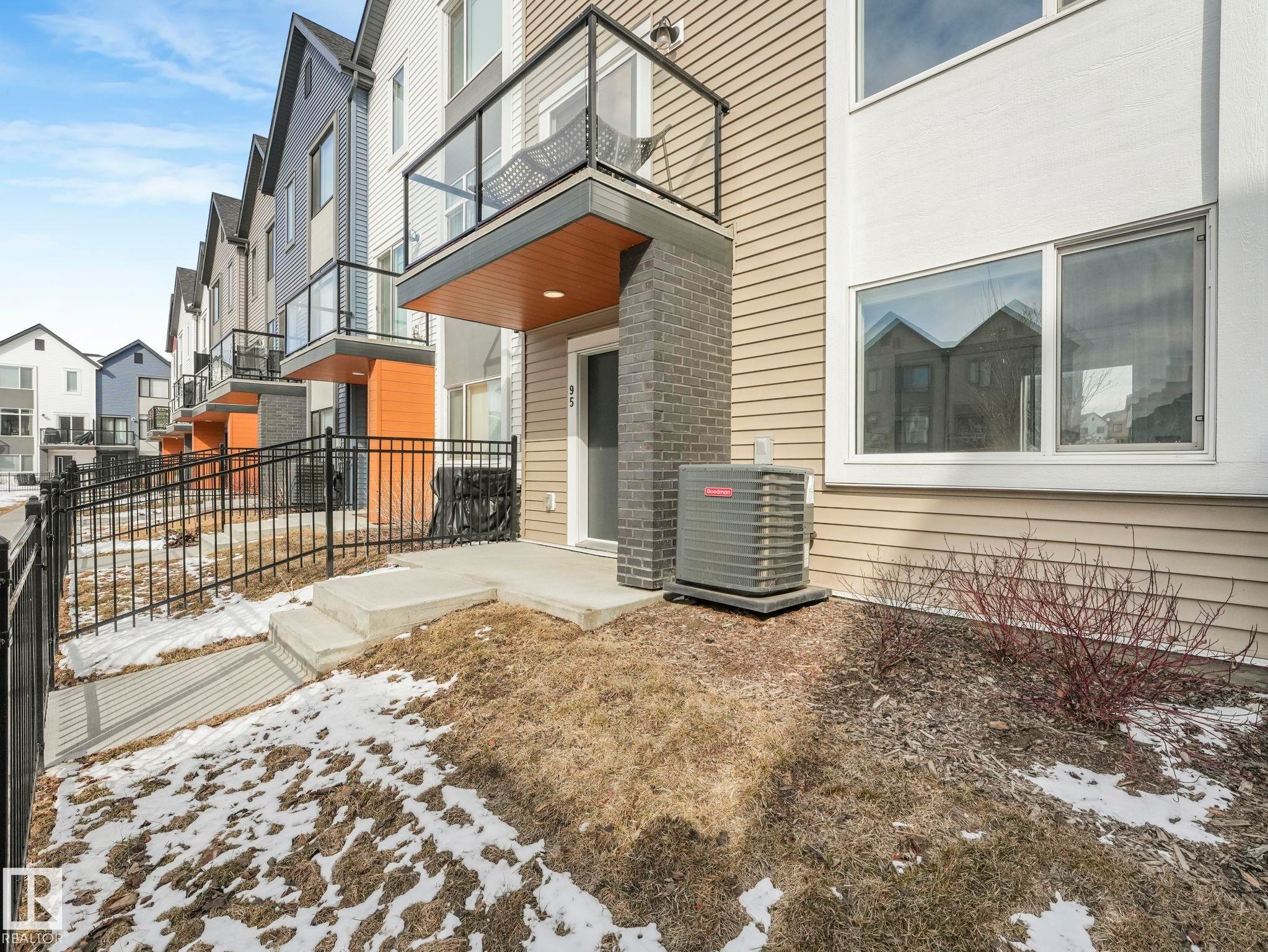 The property features modern exterior siding in varying tones, a private balcony with glass railing, and a ground-level patio area - 95 1010 Rabbit Hill Road, Edmonton, AB - Outdoor