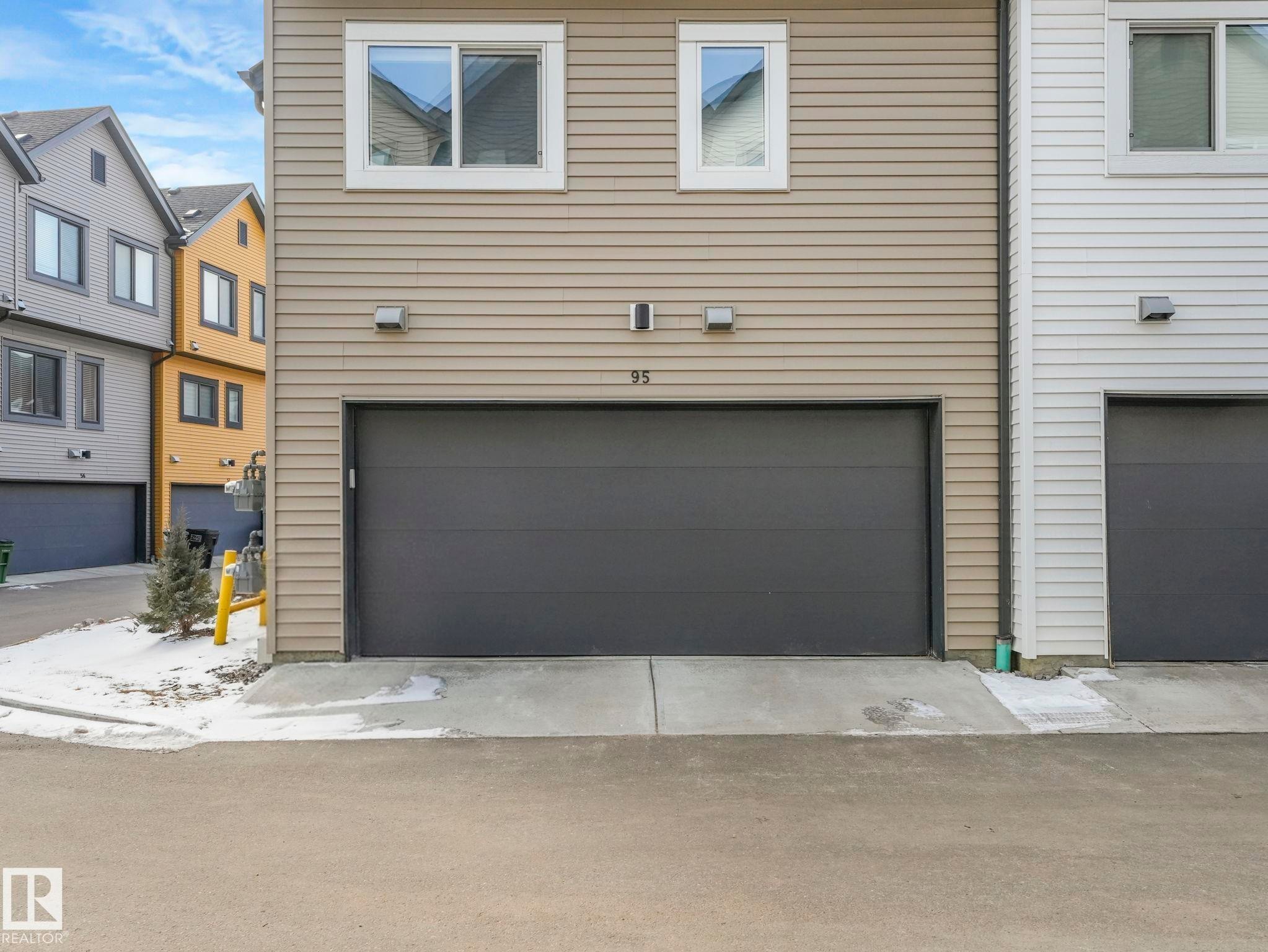 The property features a large, dark-toned garage door with two wall-mounted exterior lights - 95 1010 Rabbit Hill Road, Edmonton, AB - Outdoor With Exterior