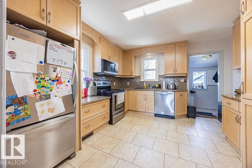 The kitchen features light wood cabinetry, stainless steel appliances, granite countertops, and tile flooring - 8736 76 Avenue, Edmonton, AB - Indoor Photo Showing Kitchen