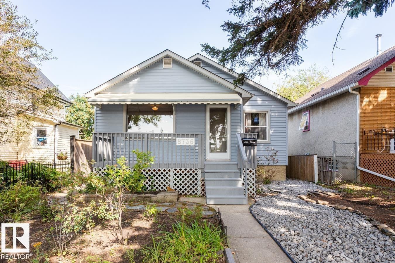 The property features light blue siding, a covered front porch with a railing, and steps leading to the front door - 8736 76 Avenue, Edmonton, AB - Outdoor With Deck Patio Veranda