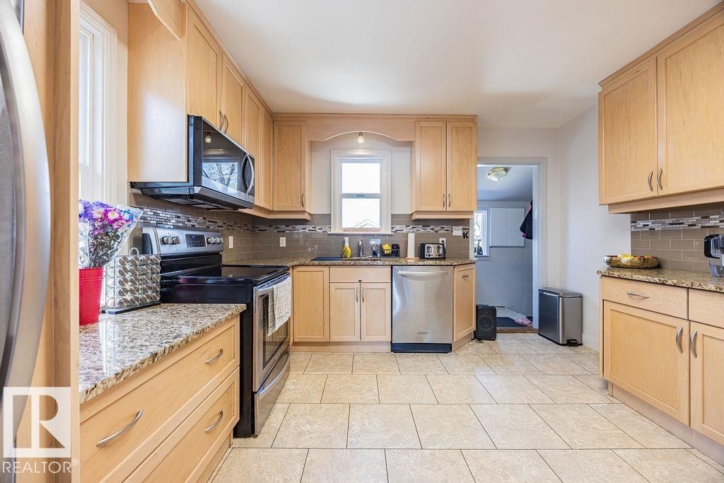 The kitchen features light wood cabinetry, stone countertops, stainless steel appliances, and a tiled floor - 8736 76 Avenue, Edmonton, AB - Indoor Photo Showing Kitchen