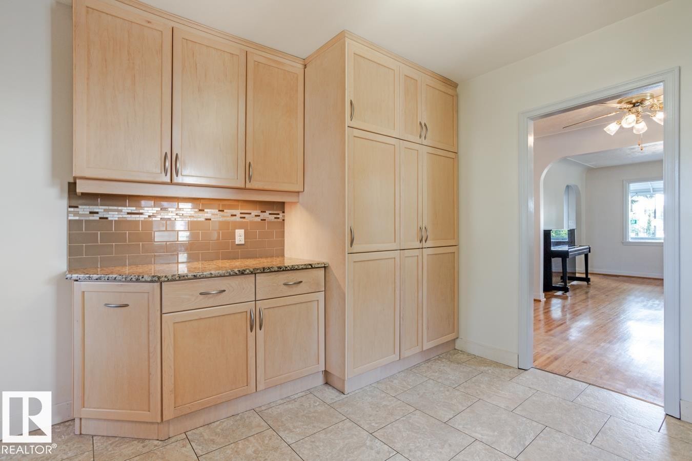Kitchenette area featuring light wood cabinetry with silver hardware, a granite countertop, and a tiled backsplash - 8736 76 Avenue, Edmonton, AB - Indoor