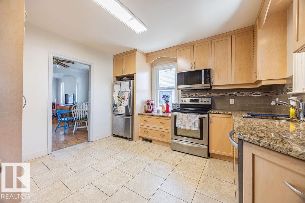 The kitchen features light wood cabinetry, stainless steel appliances, granite countertops, and tile flooring - 8736 76 Avenue, Edmonton, AB - Indoor Photo Showing Kitchen