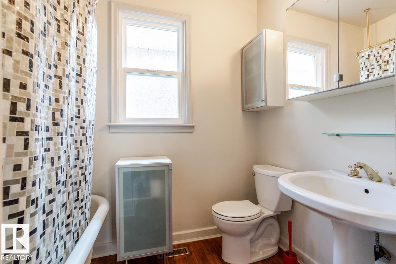 Bathroom featuring a white pedestal sink with brass-toned fixtures, a toilet, a window, and a storage cabinet - 8736 76 Avenue, Edmonton, AB - Indoor Photo Showing Bathroom