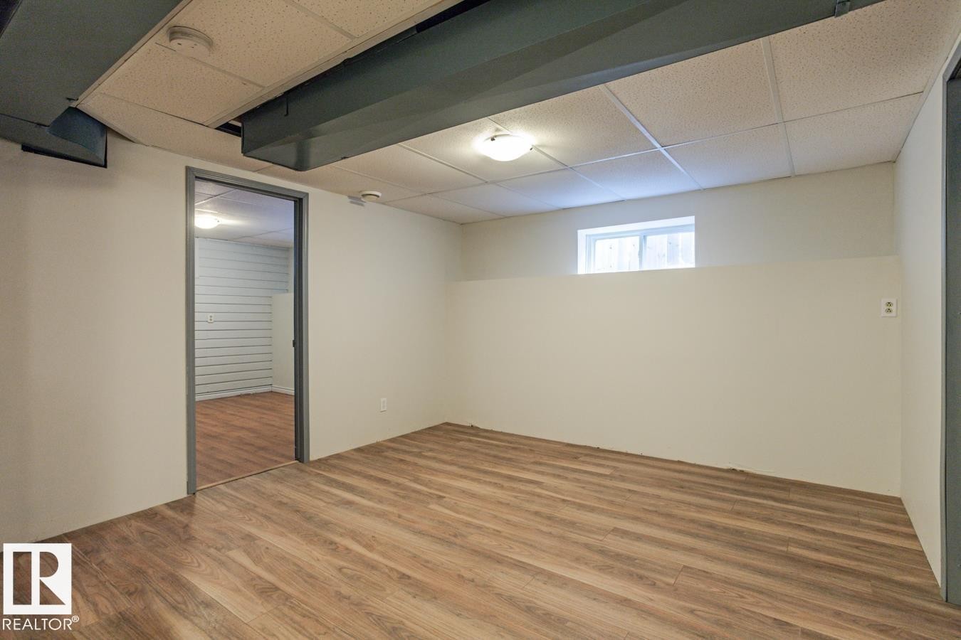 The property features a room with wood-style flooring, a drop ceiling, and a window providing natural light - 8736 76 Avenue, Edmonton, AB - Indoor