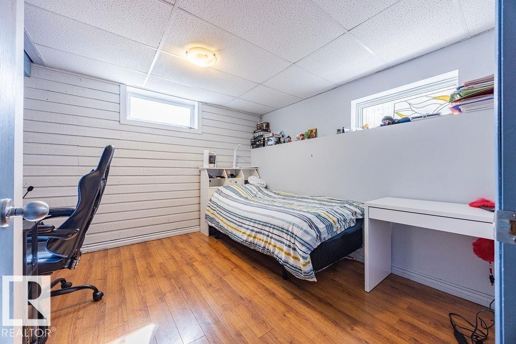 This room features wood-style flooring, white paneled walls, and a window providing natural light - 8736 76 Avenue, Edmonton, AB - Indoor Photo Showing Bedroom
