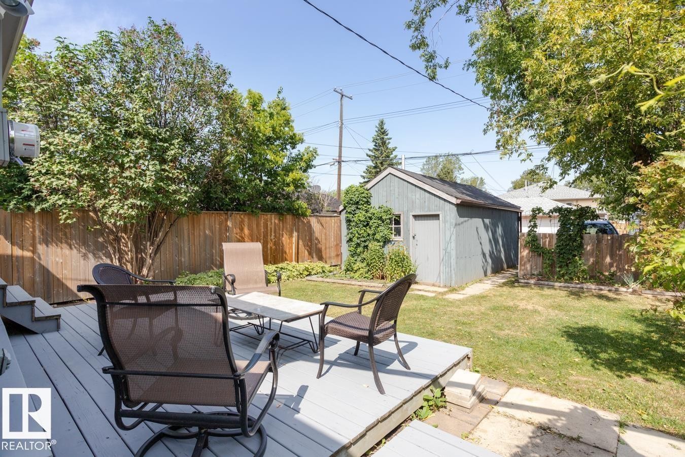 The property features a spacious backyard with a deck, a lawn, and mature trees, offering a private outdoor retreat. Wooden decks removed and concrete poured - 8736 76 Avenue, Edmonton, AB - Outdoor With Deck Patio Veranda