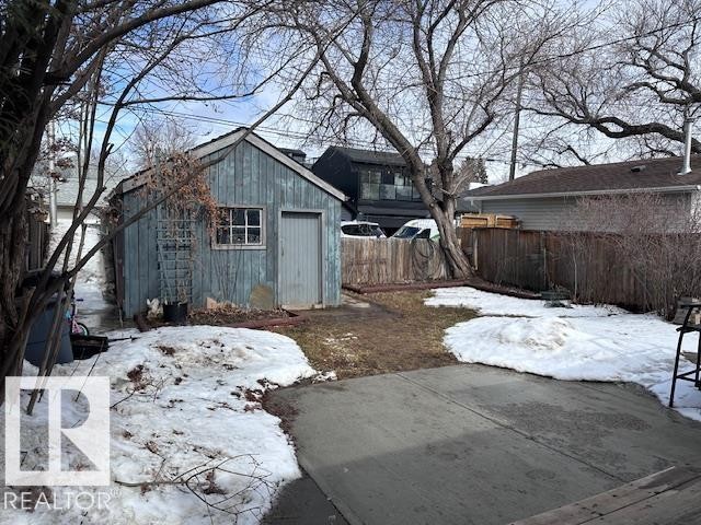 The property features a backyard with a concrete patio area, a wooden fence, and mature trees - 8736 76 Avenue, Edmonton, AB - Outdoor