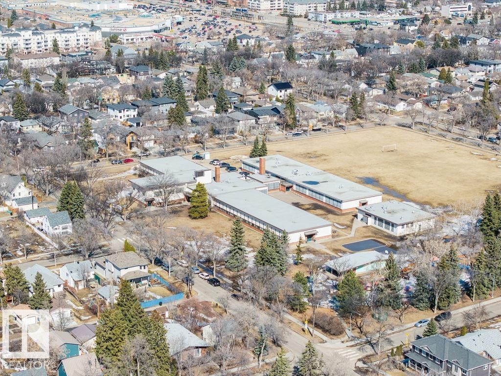 Aerial view of the surrounding neighborhood, featuring residential properties, a large open field, and several buildings with flat roofs - 8736 76 Avenue, Edmonton, AB - Outdoor With View