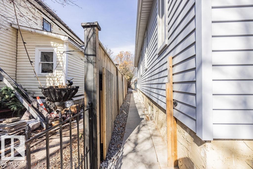 The property features light-colored siding and a concrete walkway alongside a wooden fence - 8736 76 Avenue, Edmonton, AB - With Exterior