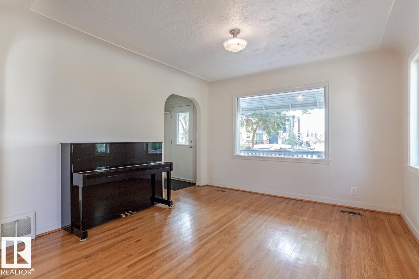 This interior space features hardwood floors, white walls, and a large window providing natural light - 8736 76 Avenue, Edmonton, AB - Indoor Photo Showing Other Room