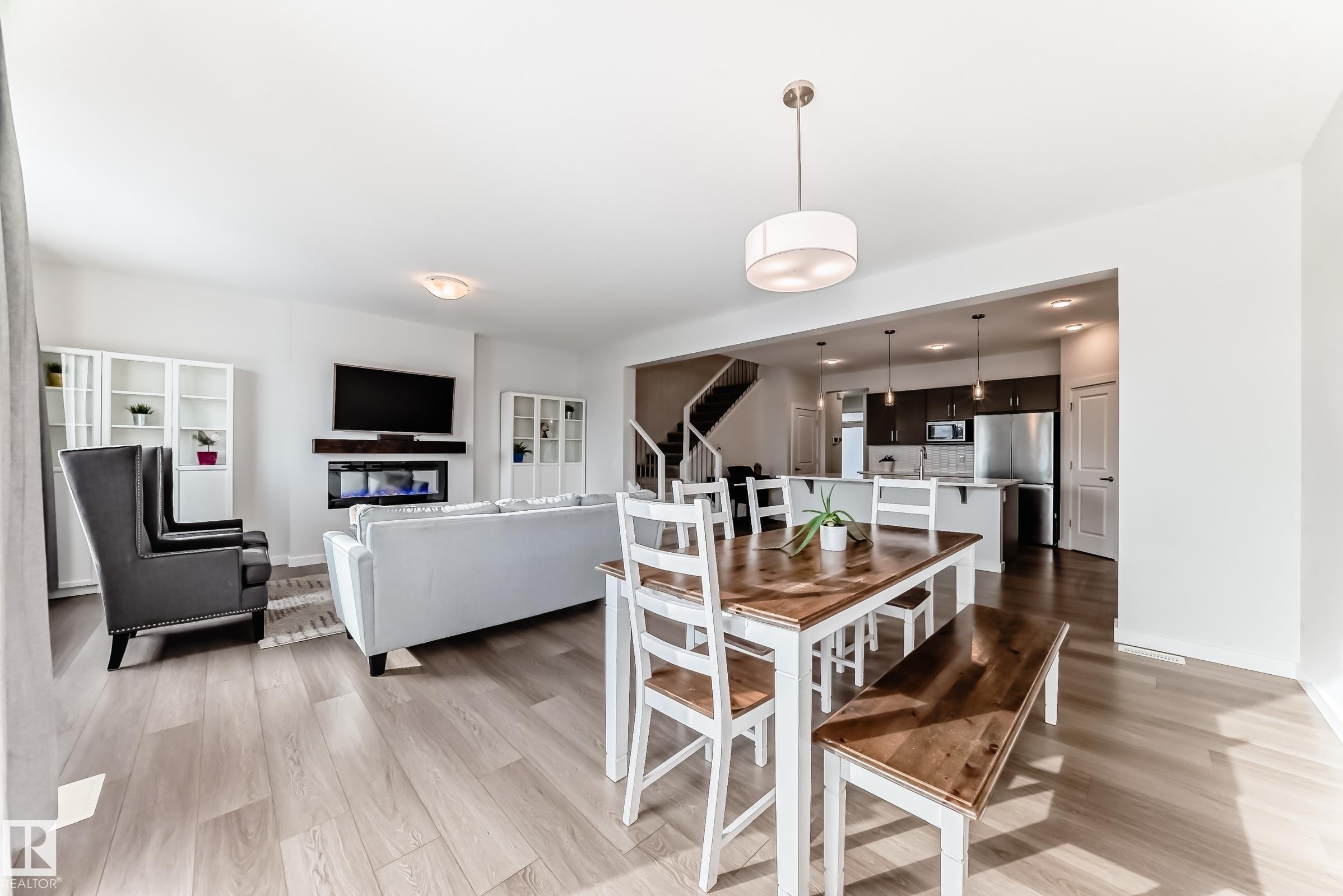 This open-concept living space features light-toned flooring, a dining area with a wood-top table, and a living area with a fireplace - 2935 Chokecherry Common, Edmonton, AB - Indoor Photo Showing Other Room
