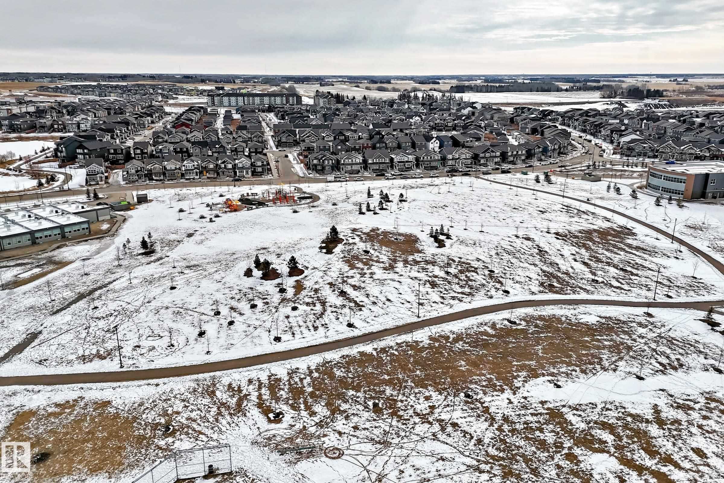 Aerial view showcasing a residential area featuring numerous detached properties, a public park with walking paths, and additional buildings in the background - 2935 Chokecherry Common, Edmonton, AB - Outdoor With View