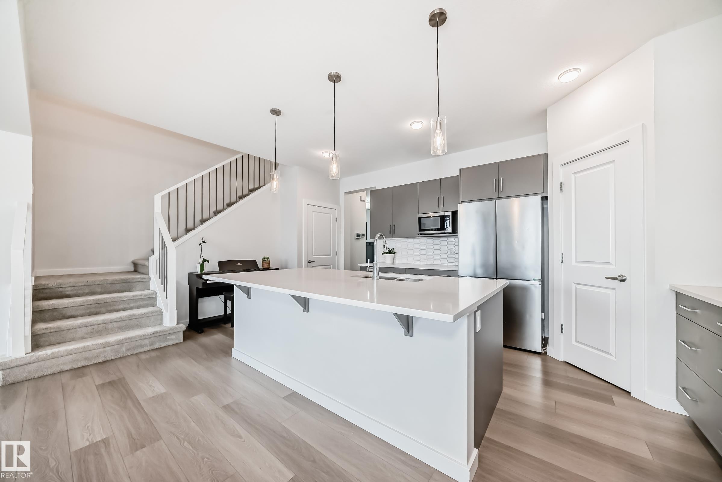 Open concept living space featuring a contemporary kitchen island with a white countertop and pendant lighting, stainless steel appliances, and wood-look flooring - 2935 Chokecherry Common, Edmonton, AB - Indoor Photo Showing Kitchen With Upgraded Kitchen