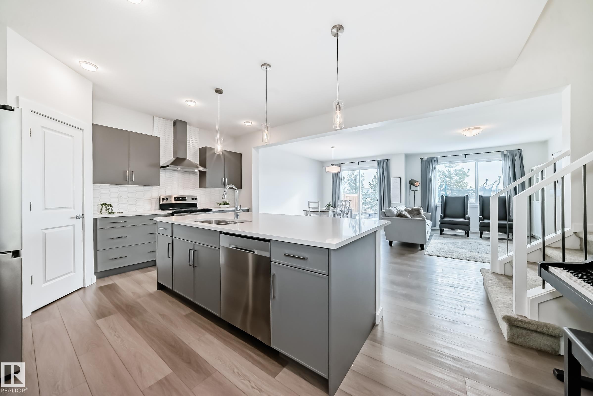 The kitchen features a large island with a sink, grey cabinetry, stainless steel appliances, and a tiled backsplash - 2935 Chokecherry Common, Edmonton, AB - Indoor Photo Showing Kitchen With Upgraded Kitchen