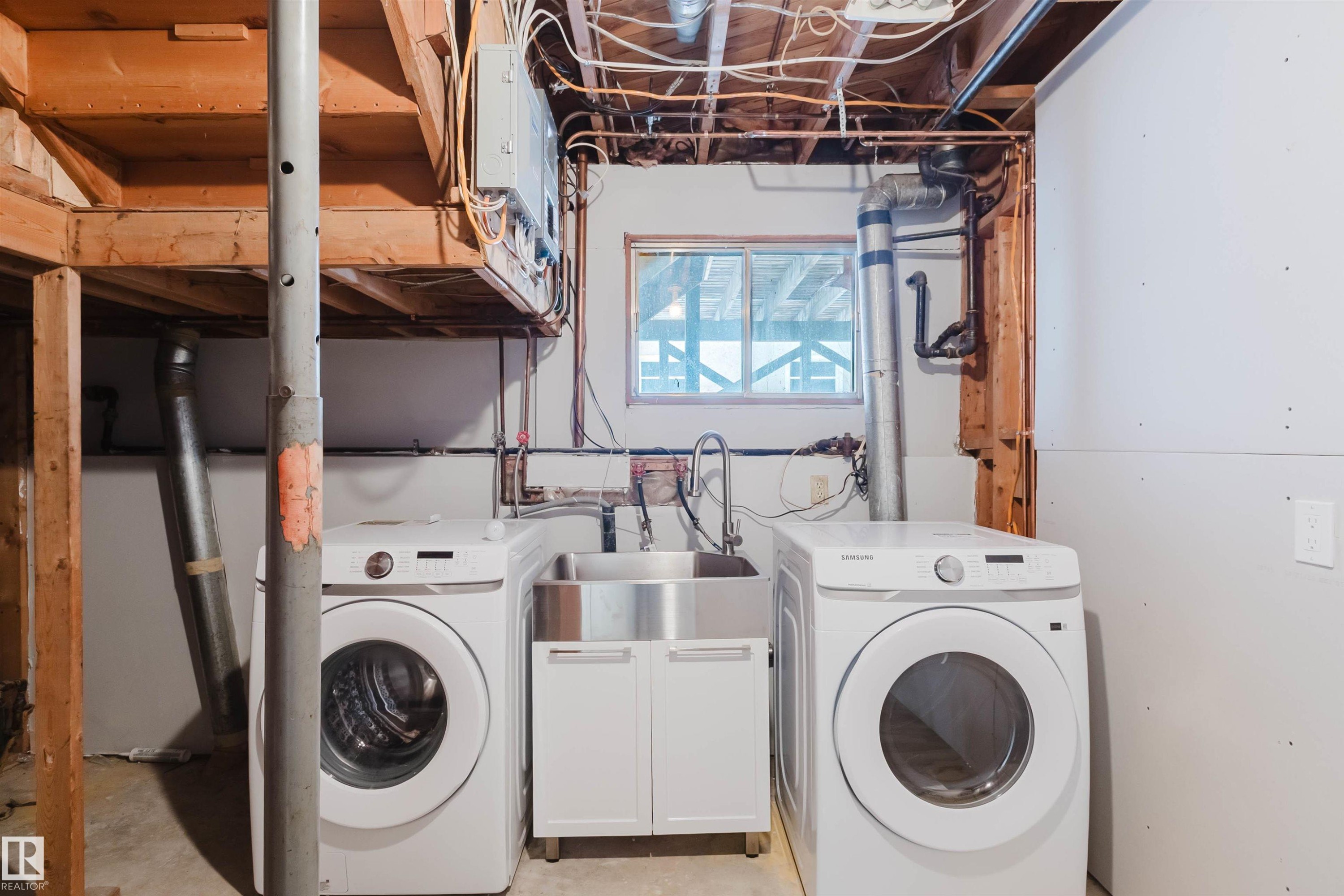 Laundry area featuring two front-loading machines, a stainless steel utility sink with a cabinet, and a window providing natural light - 11528 42 Avenue, Edmonton, AB - Indoor Photo Showing Laundry Room