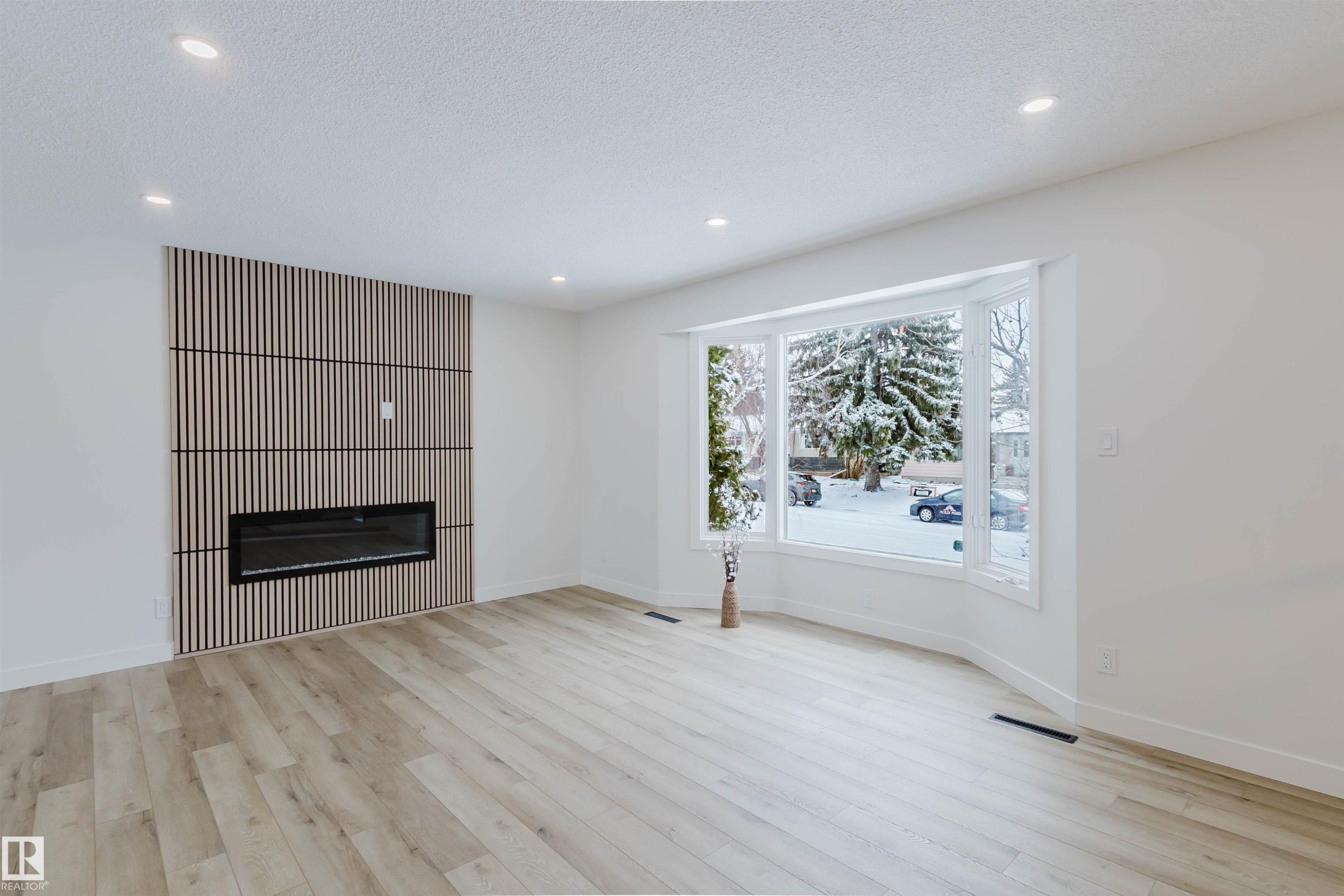 The property features an inviting living area with light-toned flooring, recessed lighting, and a modern fireplace integrated into a textured wall panel - 11528 42 Avenue, Edmonton, AB - Indoor