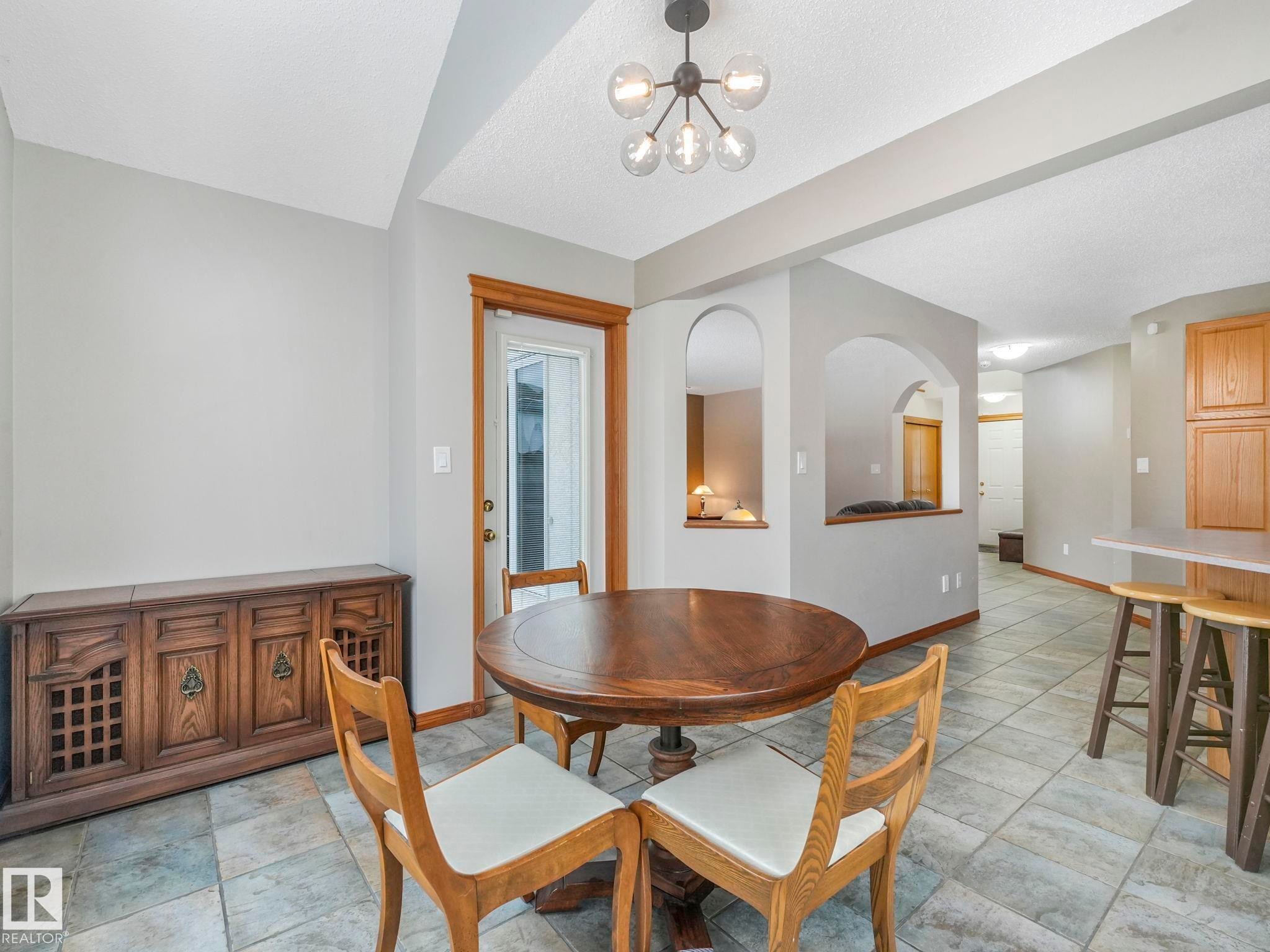 This dining area features a modern ceiling light fixture, tile flooring, and a door providing exterior access - 11704 11 Avenue, Edmonton, AB - Indoor Photo Showing Dining Room