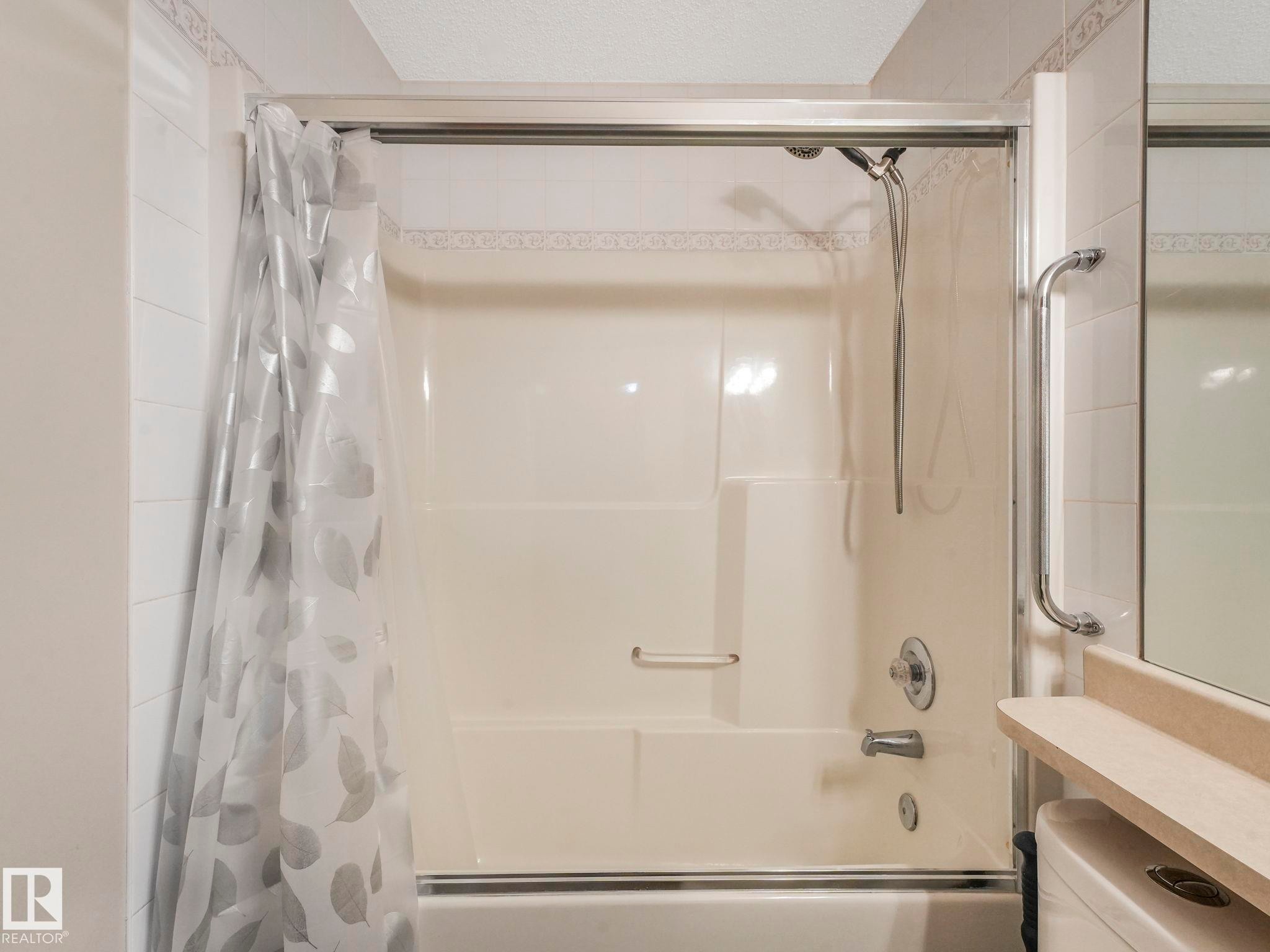 Bathroom with a shower and bathtub combination unit, featuring a clear shower curtain with a leaf pattern - 11704 11 Avenue, Edmonton, AB - Indoor Photo Showing Bathroom