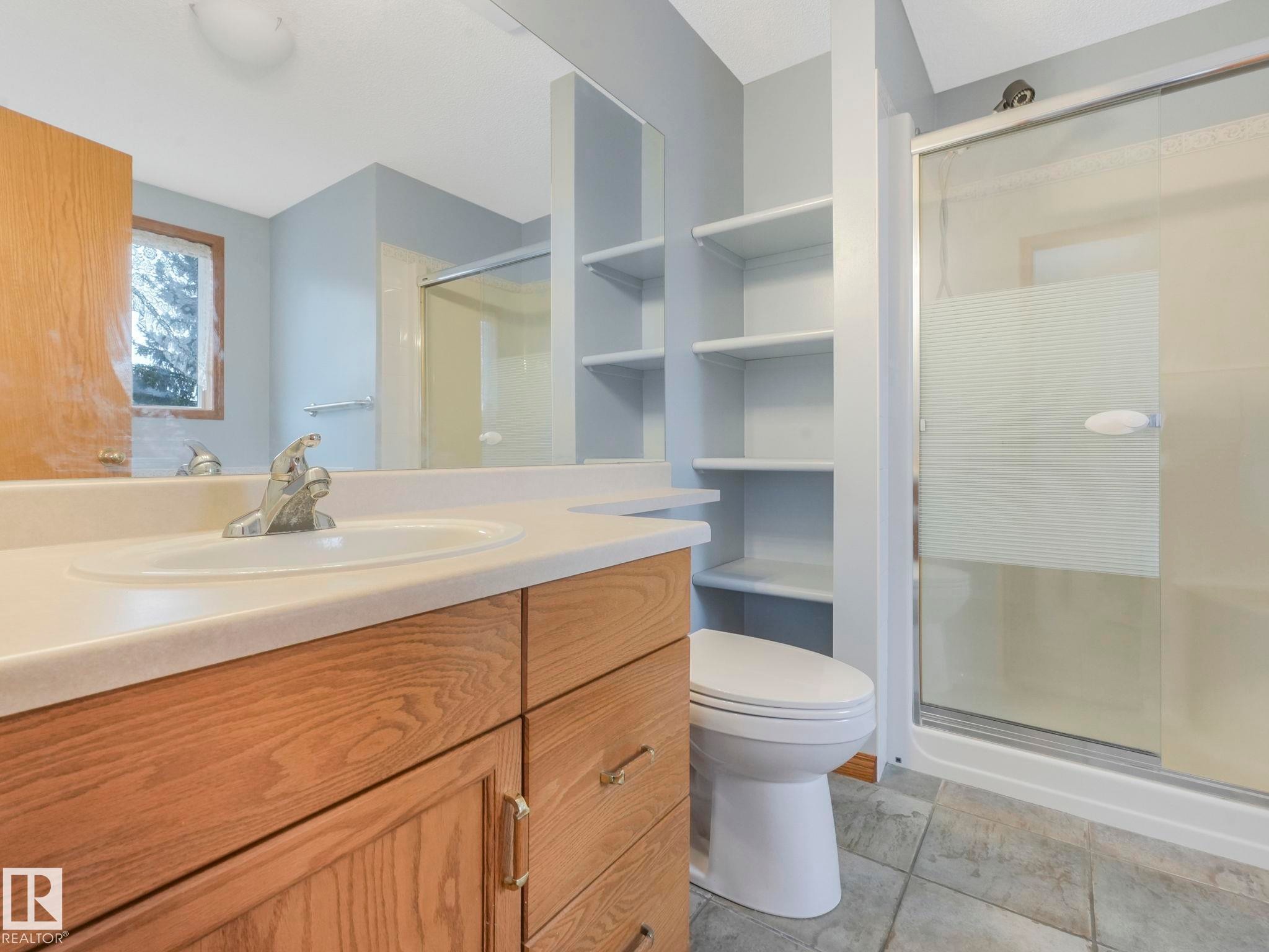 Bathroom featuring a light-colored vanity with an integrated sink and chrome faucet, built-in shelving, and a glass-enclosed shower - 11704 11 Avenue, Edmonton, AB - Indoor Photo Showing Bathroom