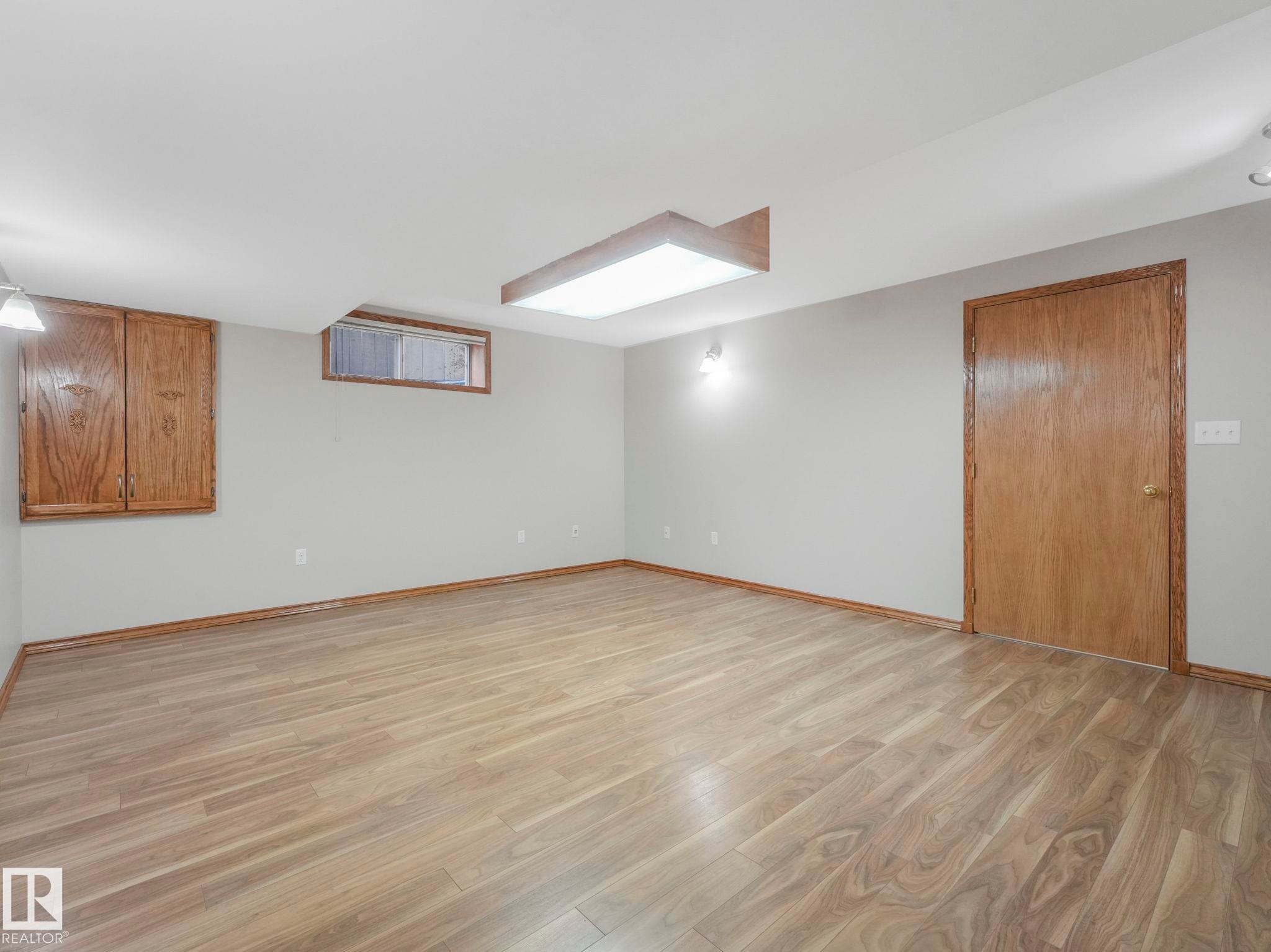 Spacious room featuring light-colored flooring, light-toned walls, and a wooden door with matching trim - 11704 11 Avenue, Edmonton, AB - Indoor Photo Showing Other Room
