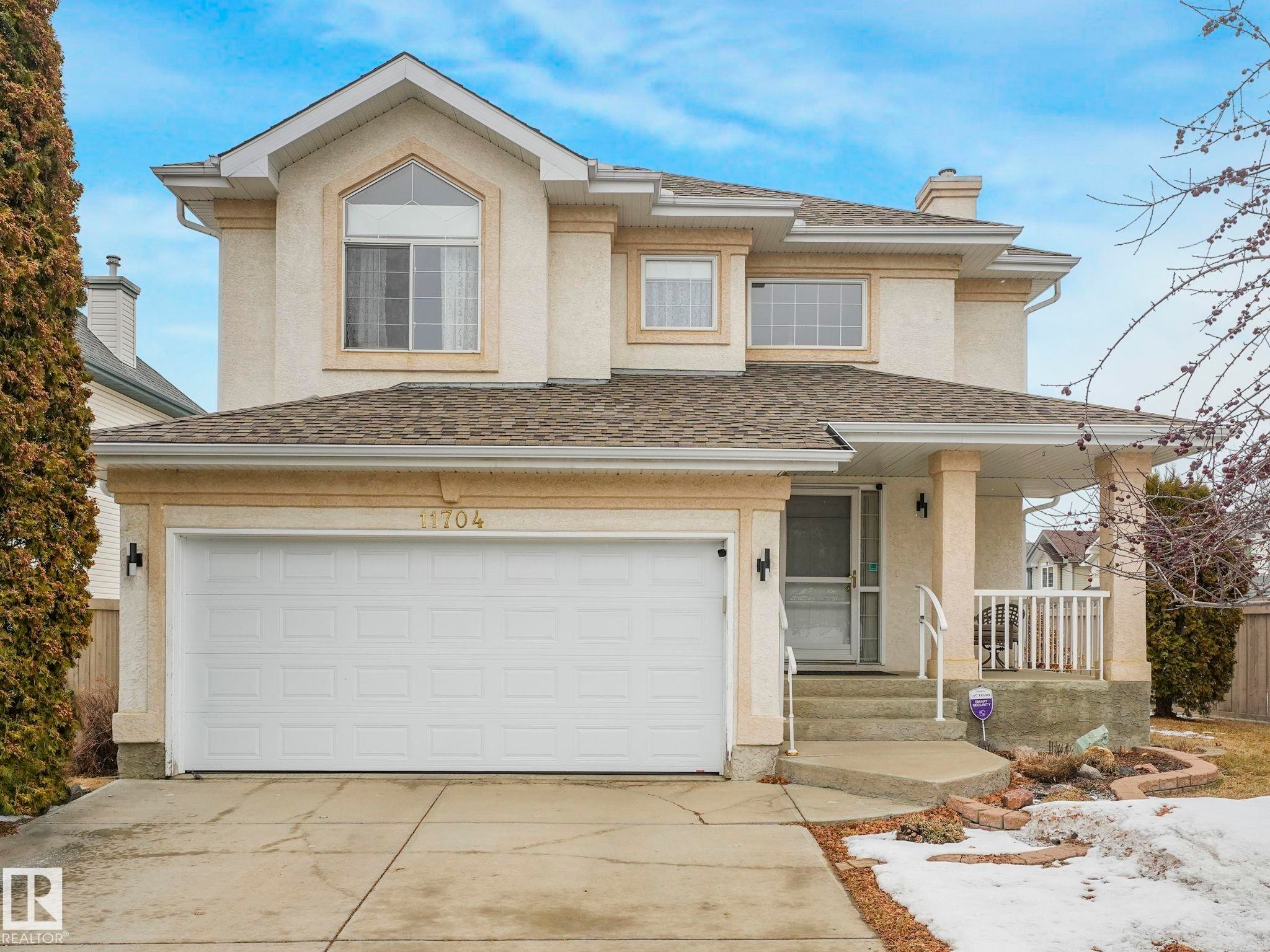 The property features a two-car garage, a covered front porch, and a light-colored exterior with decorative trim - 11704 11 Avenue, Edmonton, AB - Outdoor With Deck Patio Veranda With Facade