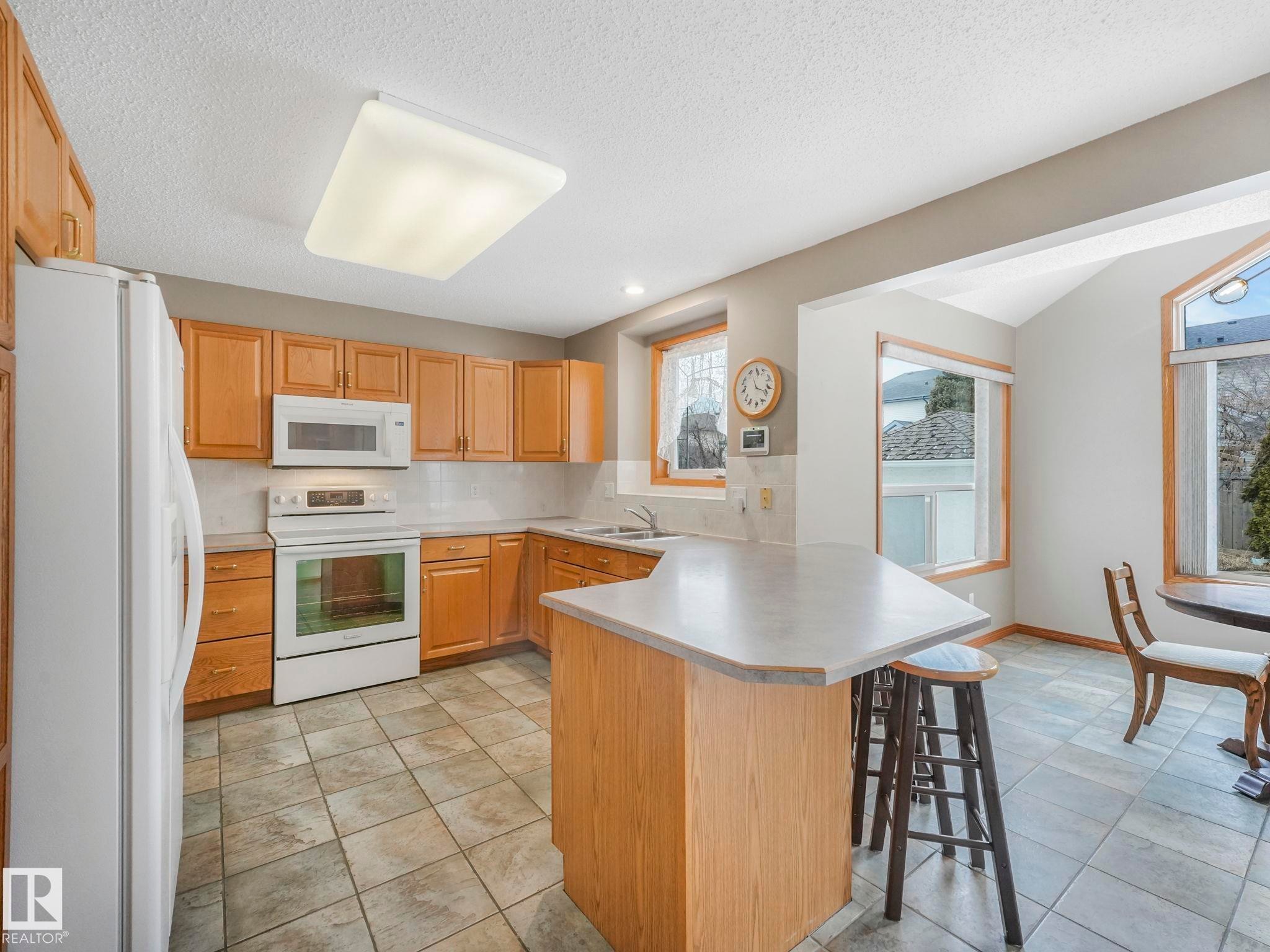 The kitchen features light wood cabinetry, white appliances, and tiled flooring - 11704 11 Avenue, Edmonton, AB - Indoor Photo Showing Kitchen With Double Sink