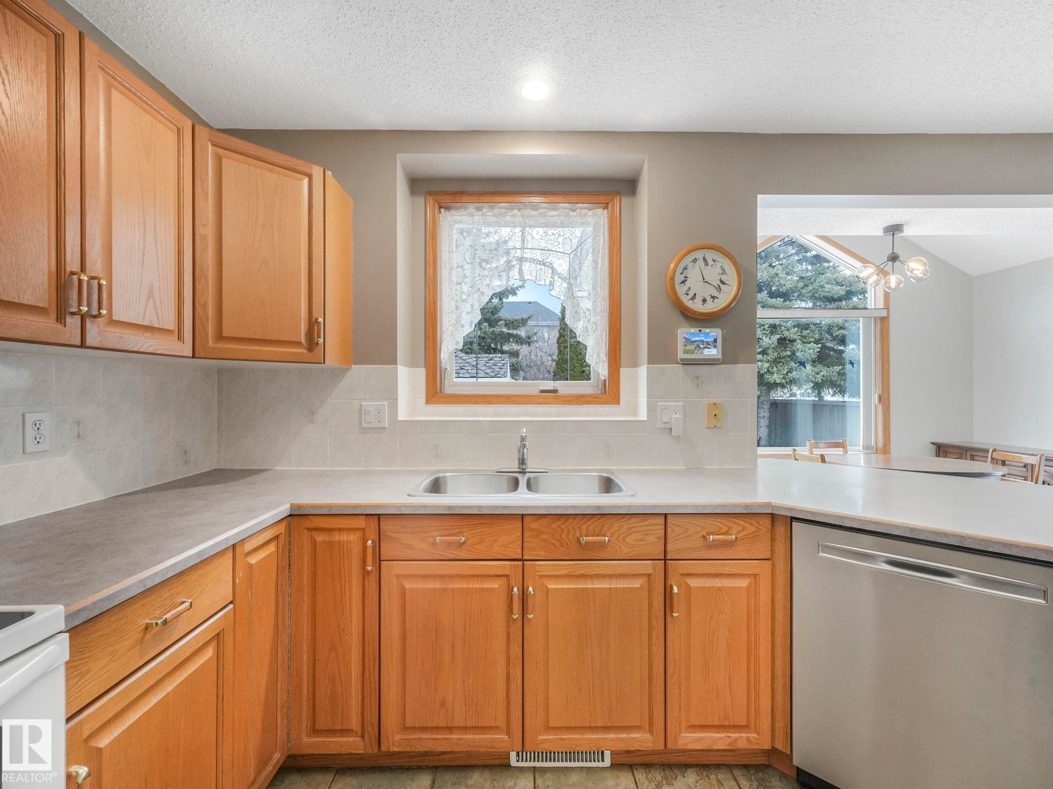 The kitchen features wood cabinetry, a double basin sink, and a stainless steel dishwasher - 11704 11 Avenue, Edmonton, AB - Indoor Photo Showing Kitchen With Double Sink