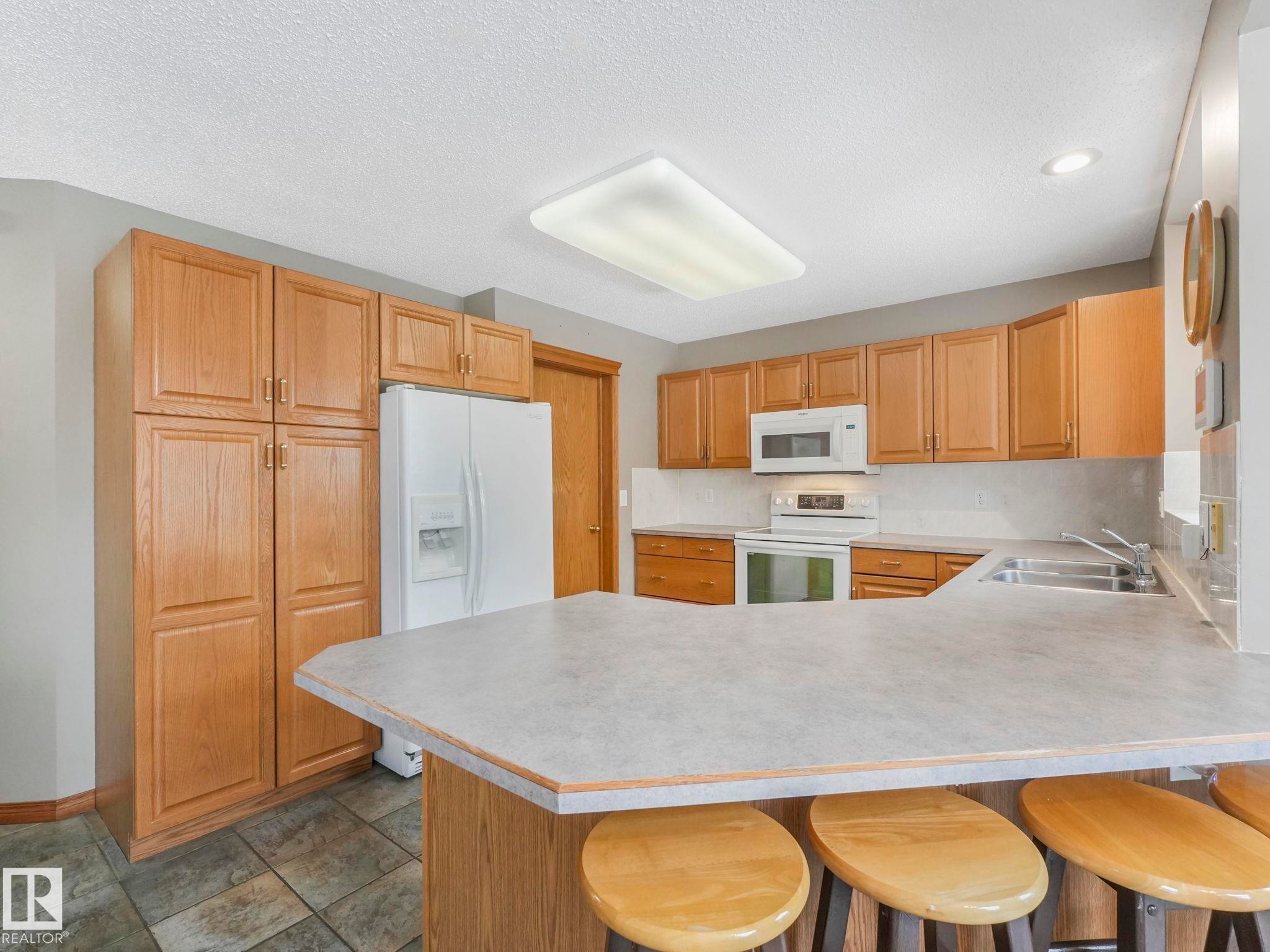 The kitchen features extensive light wood cabinetry, a white refrigerator, a white built-in microwave, and a white oven with a stovetop - 11704 11 Avenue, Edmonton, AB - Indoor Photo Showing Kitchen With Double Sink