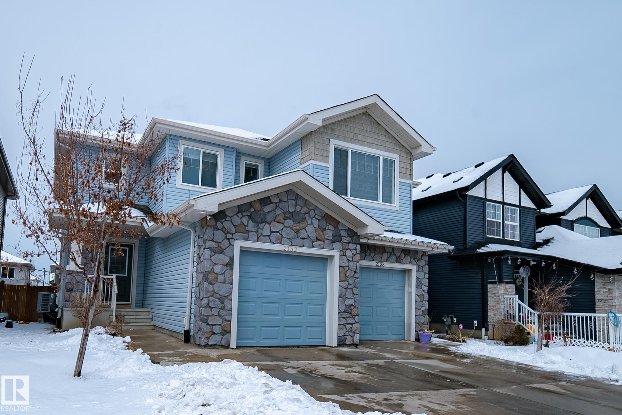 The property features a light blue exterior with stone facade accents and a double garage - 2132 52 St, Edmonton, AB - Outdoor