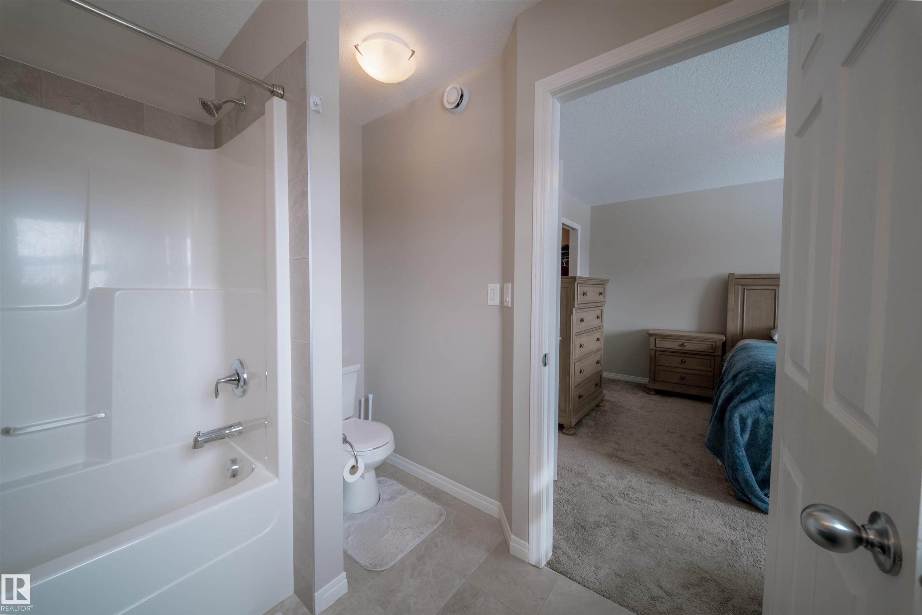 Bathroom featuring a white bathtub with an integrated shower, a toilet, and light-colored floor tiles - 2132 52 St, Edmonton, AB - Indoor Photo Showing Bathroom