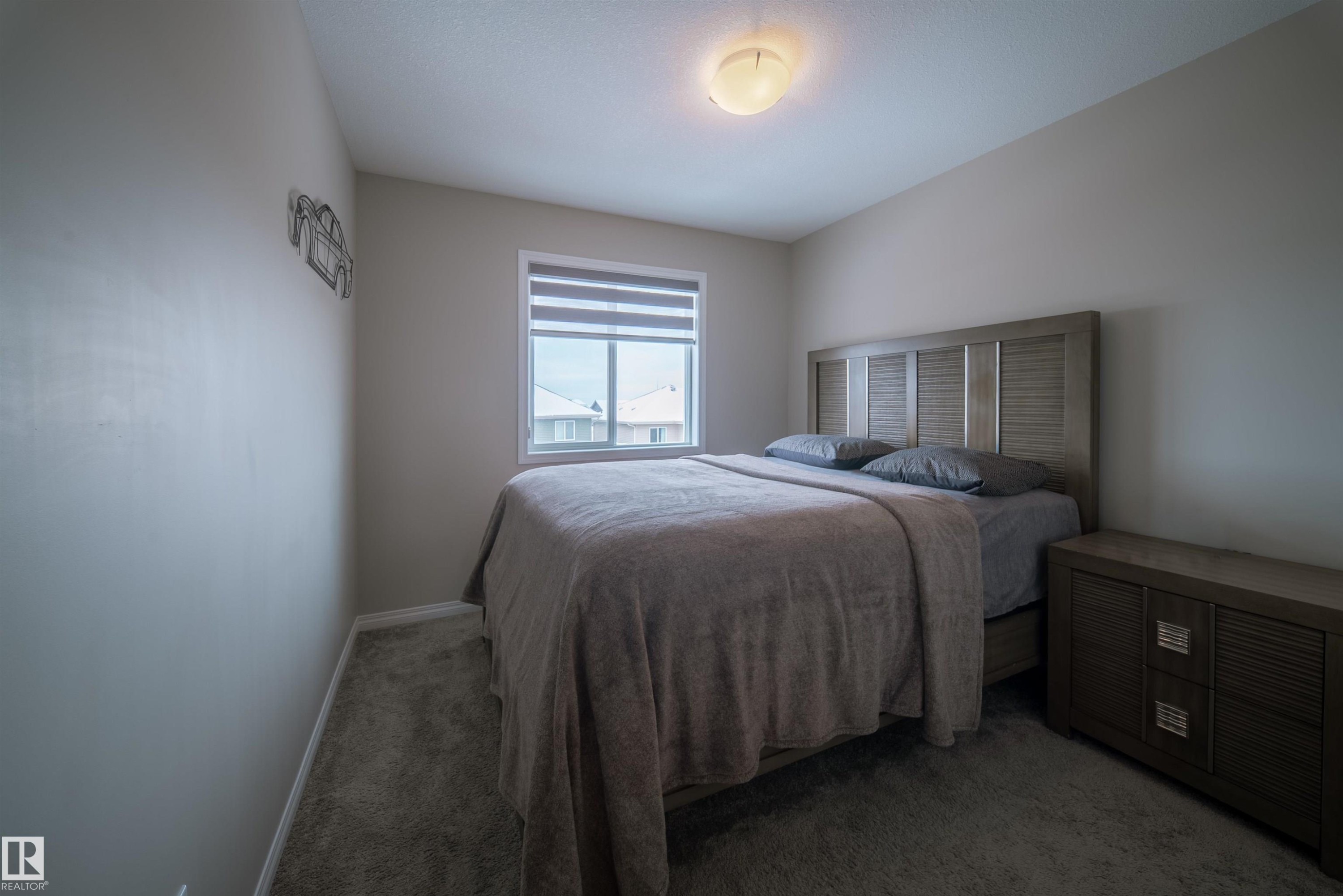 This bedroom features wall-to-wall carpeting, a window with blinds, and a ceiling light fixture - 2132 52 St, Edmonton, AB - Indoor Photo Showing Bedroom