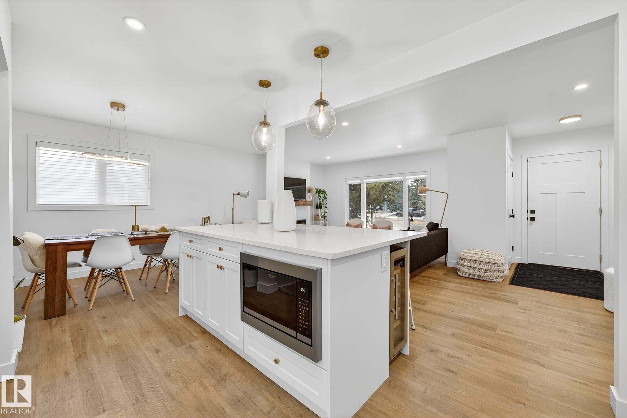 Kitchen with a center island, stainless steel microwave, white cabinetry, hanging light fixtures, and light wood-type flooring - 8604 142 Street, Edmonton, AB - Indoor
